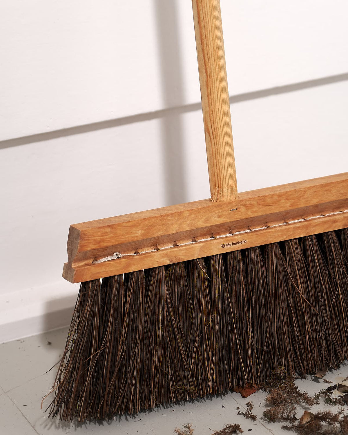 An Outdoor Broom – Birch & Bassine by Iris Hantverk with a wooden handle sitting on the floor.