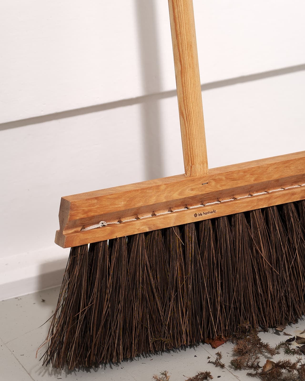 An Outdoor Broom – Birch & Bassine, made by Iris Hantverk, sitting on the floor of a room.