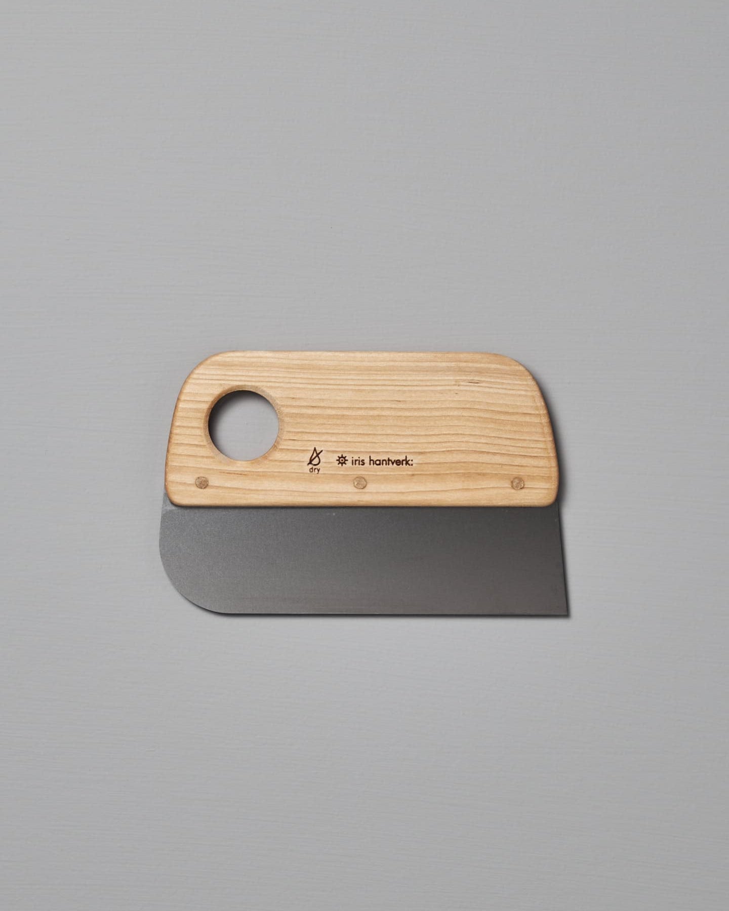 An Iris Hantverk Dough Scraper with a stainless steel blade and a circular hole in the handle, placed on a plain gray surface. This essential baking tool is perfect for all your pastry needs.