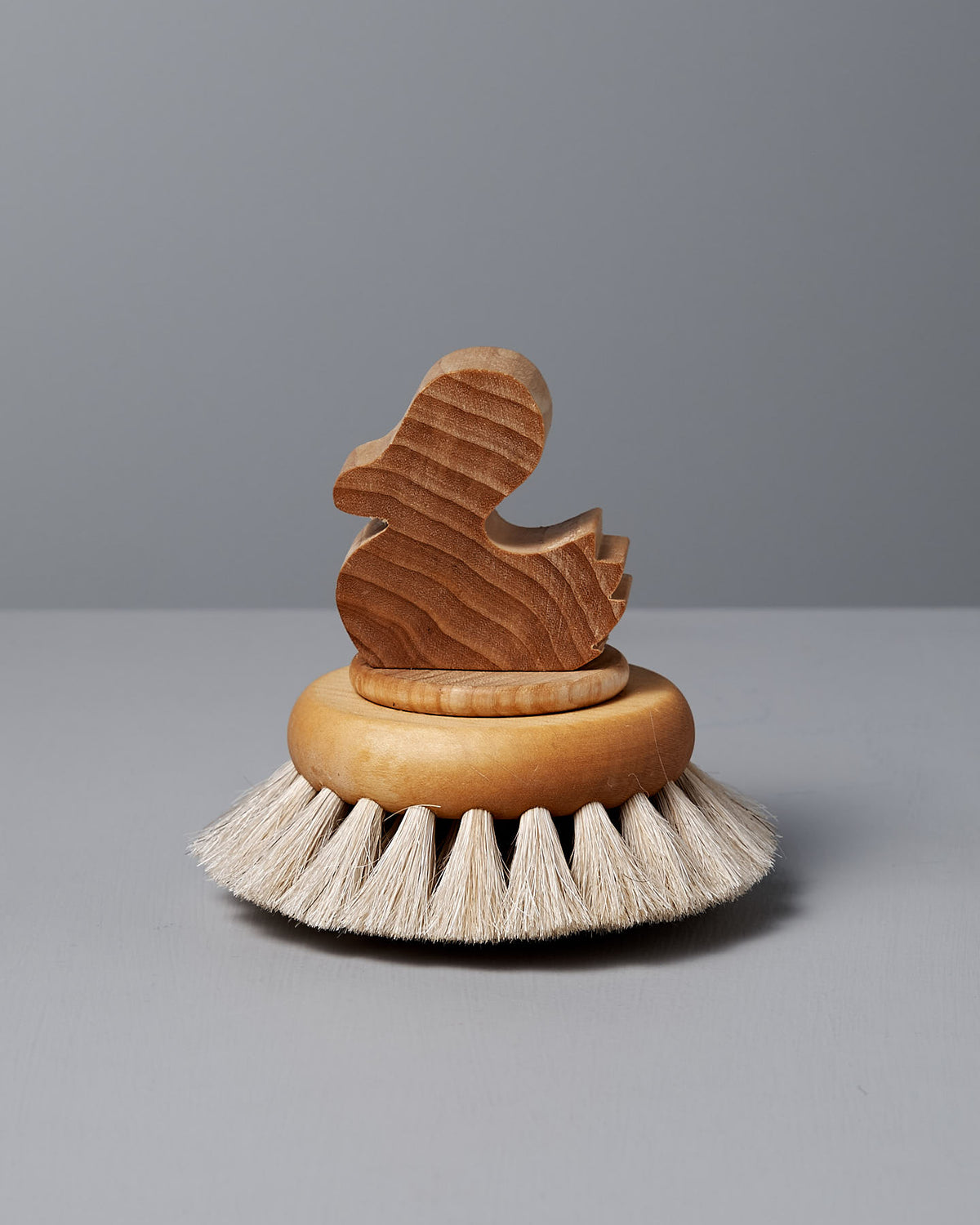 The Duck Bath Brush – Soft by Iris Hantverk is an elegant duck-shaped bath brush with a wooden handle and white bristles set against a gray surface.