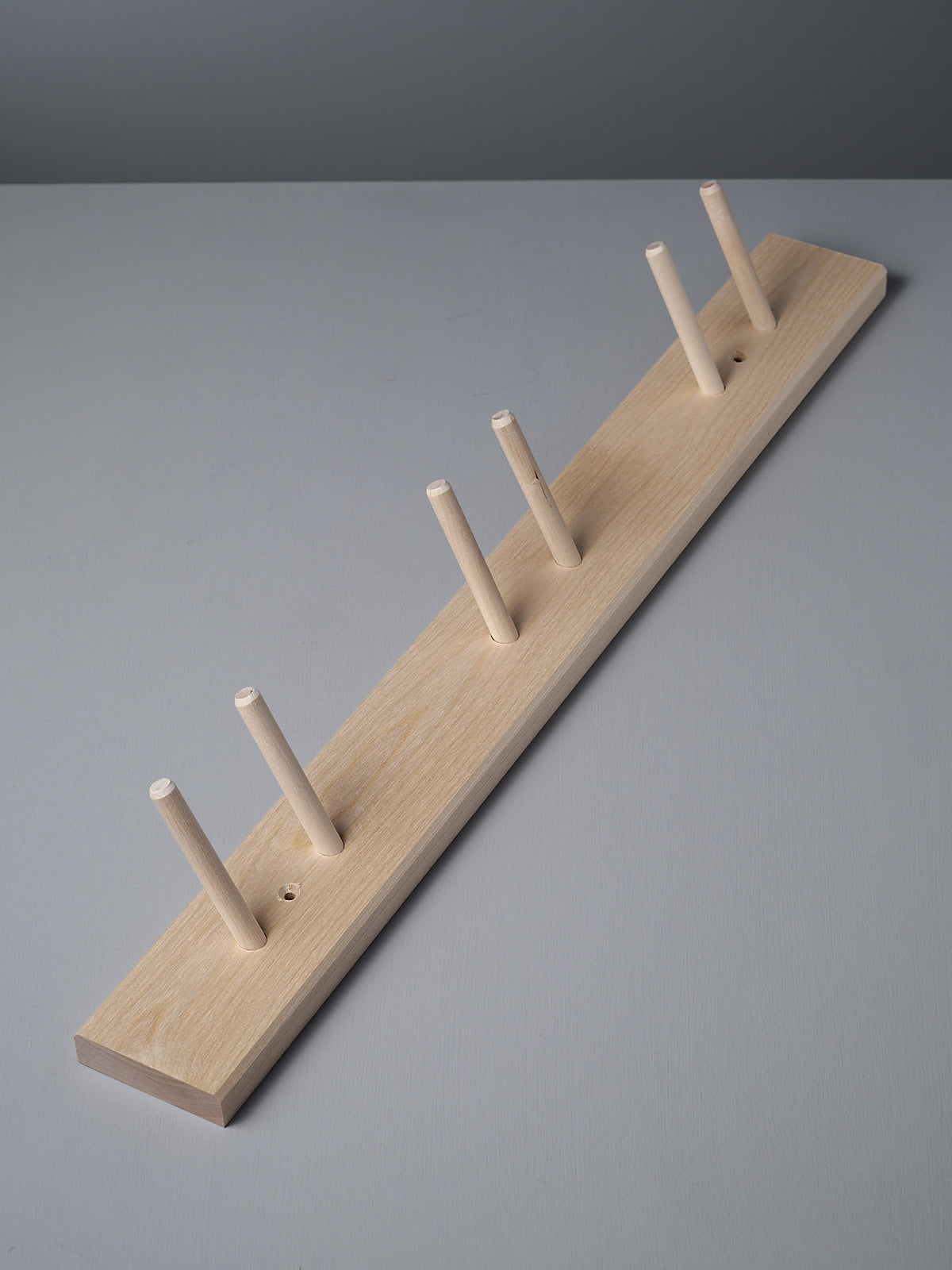 Iris Hantverk&#39;s Birchwood Garden Tool Hanger, showcasing a peg rail with six pegs, is elegantly featured on a gray surface for practical storage.