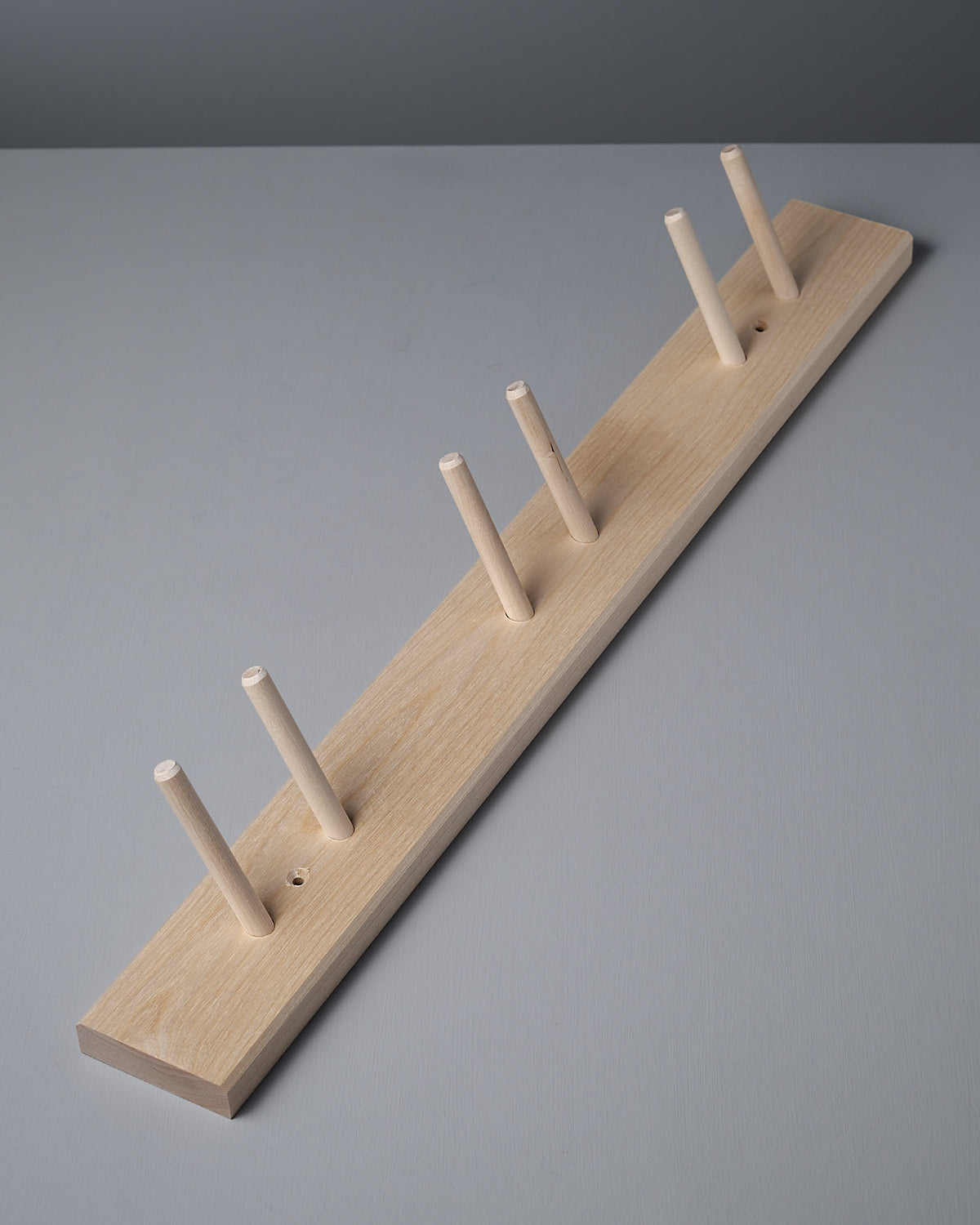 Iris Hantverk's Birchwood Garden Tool Hanger, showcasing a peg rail with six pegs, is elegantly featured on a gray surface for practical storage.
