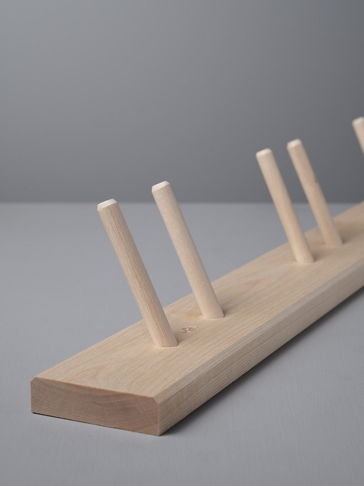 Introducing the Iris Hantverk &#39;Birchwood Garden Tool Hanger,&#39; a Shaker-inspired wooden rack with five angled pegs set against a gray background.