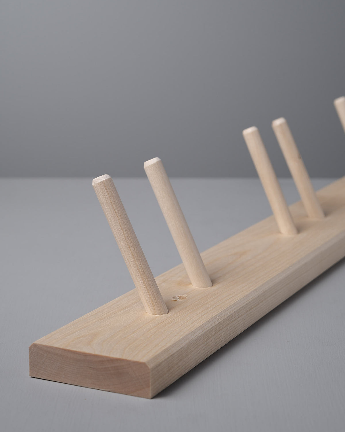 Introducing the Iris Hantverk 'Birchwood Garden Tool Hanger,' a Shaker-inspired wooden rack with five angled pegs set against a gray background.