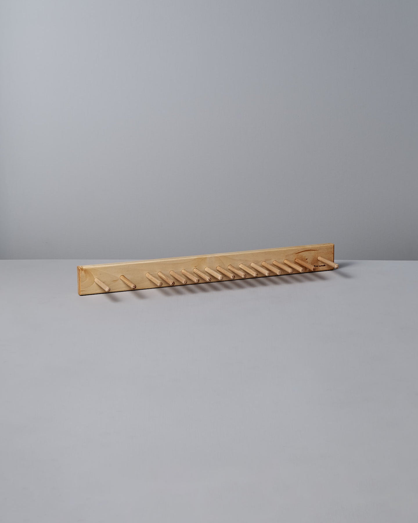 The Knopplist Hook Rack – Oiled Maple by Iris Hantverk sits elegantly on a grey surface, showcasing the craftsmanship synonymous with Iris Hantverk, all set against a light grey background.