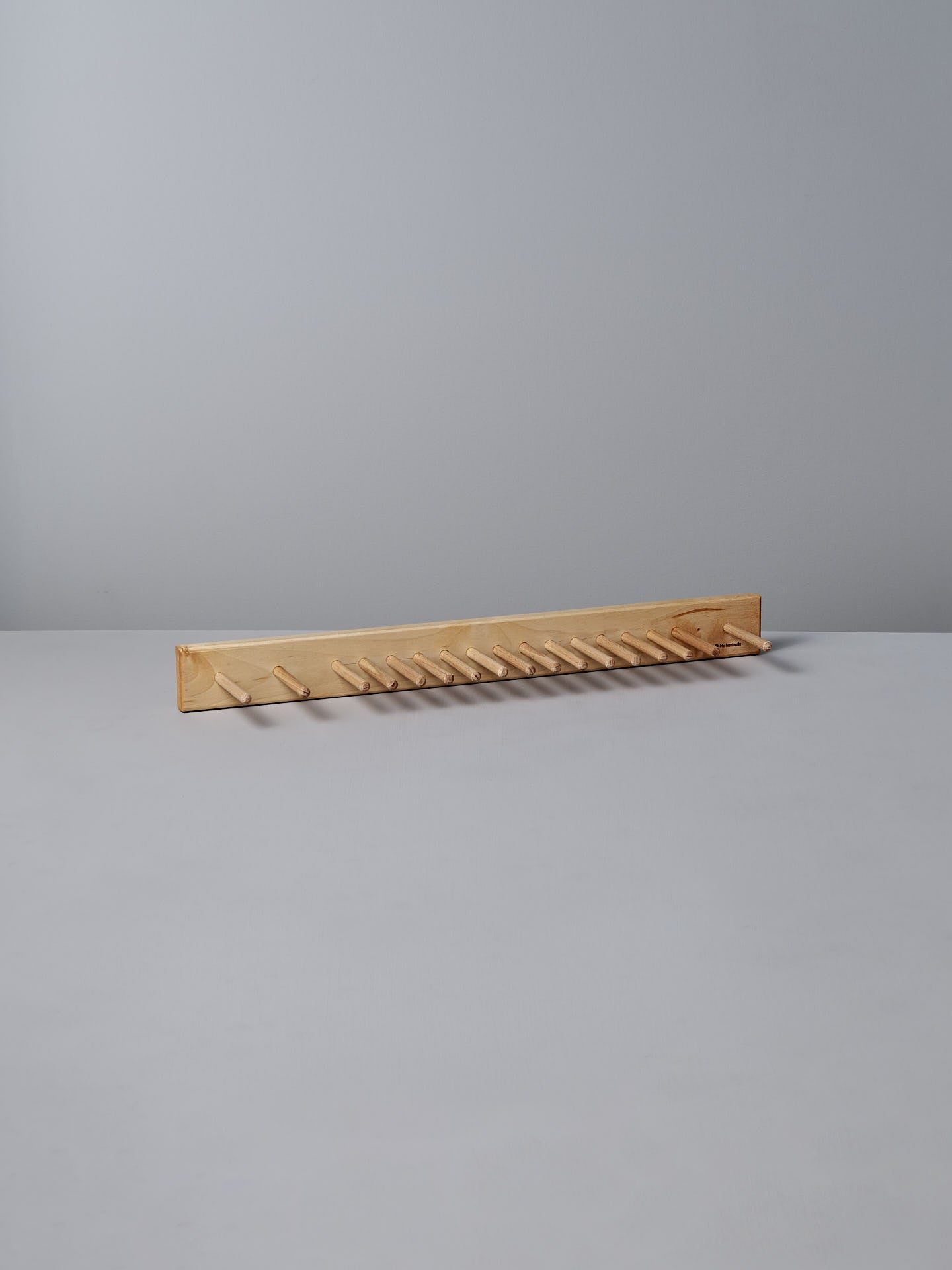 The Knopplist Hook Rack – Oiled Maple by Iris Hantverk sits elegantly on a grey surface, showcasing the craftsmanship synonymous with Iris Hantverk, all set against a light grey background.