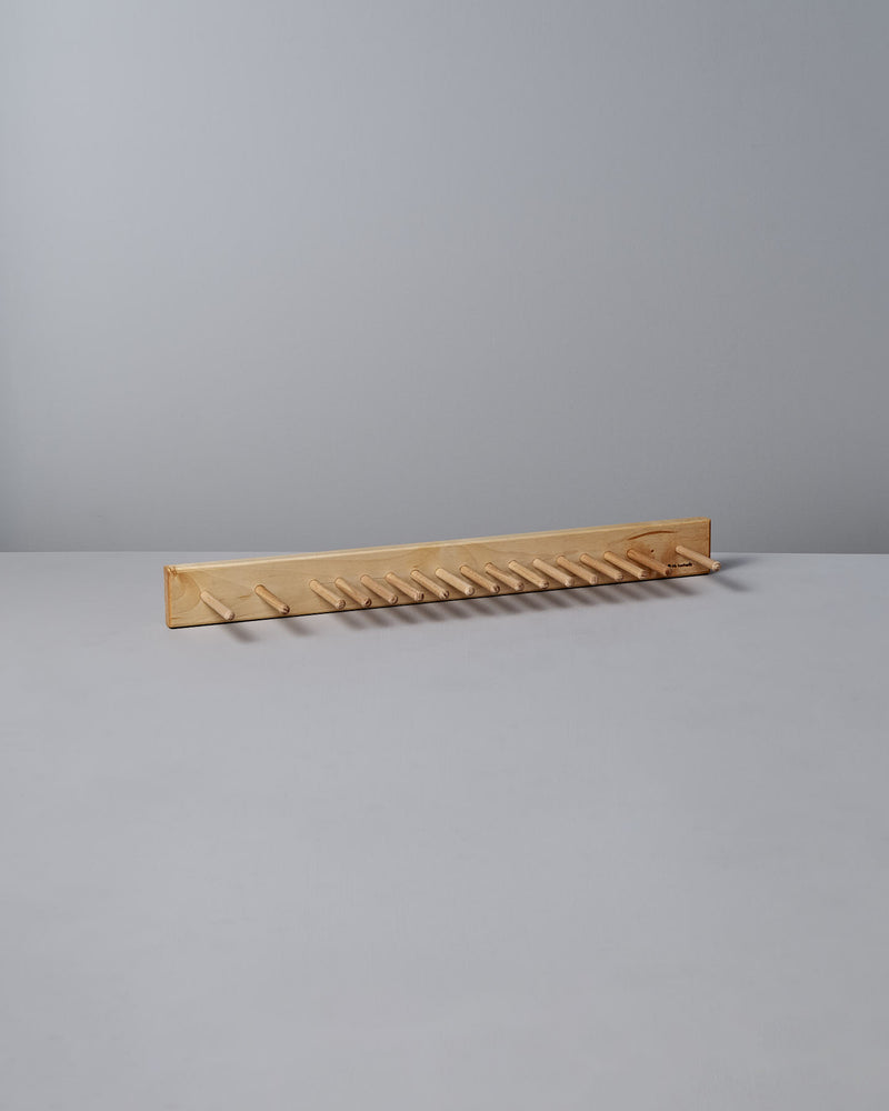 The Knopplist Hook Rack – Oiled Maple by Iris Hantverk sits elegantly on a grey surface, showcasing the craftsmanship synonymous with Iris Hantverk, all set against a light grey background.