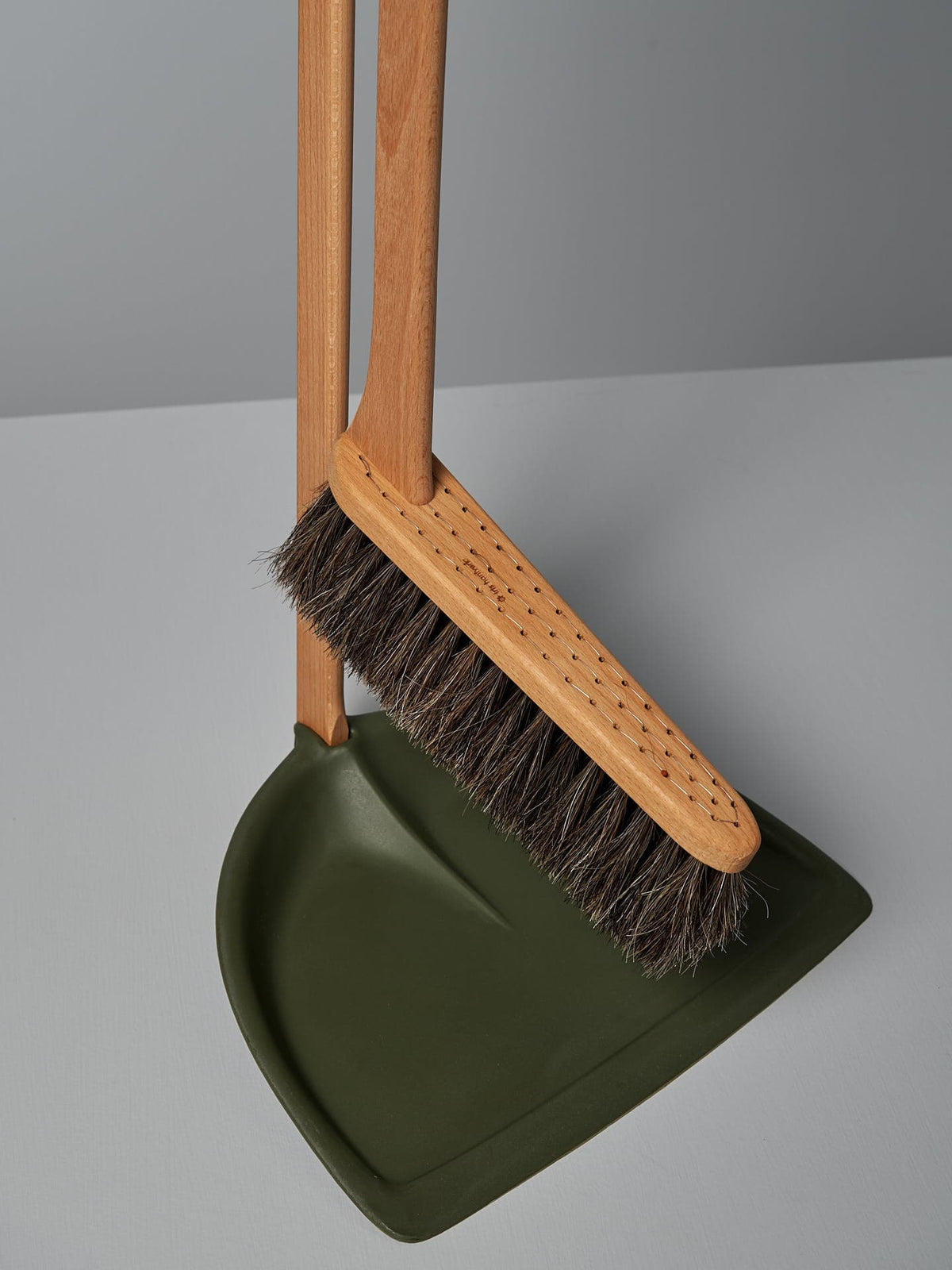 An Iris Hantverk Long Handled Dustpan &amp; Brush Set – Moss Green featuring a green bio-polyethylene dustpan and a natural horsehair brush is placed against a grey background.