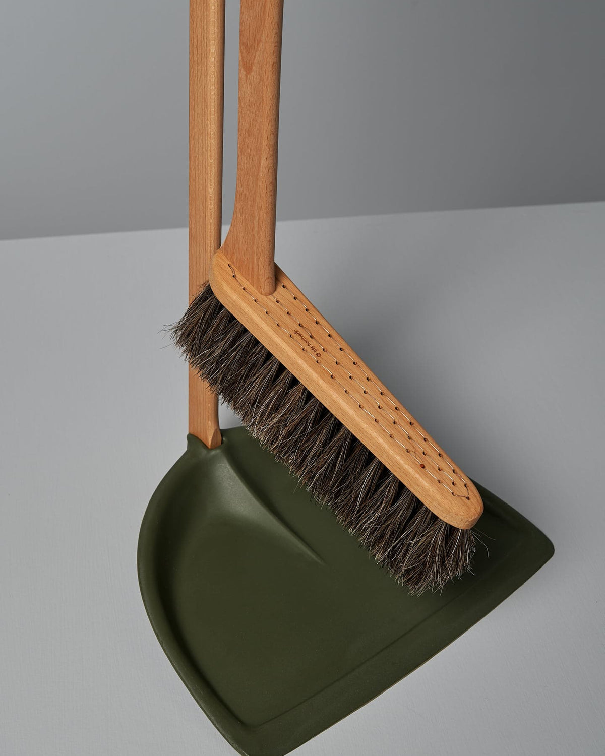 An Iris Hantverk Long Handled Dustpan & Brush Set – Moss Green featuring a green bio-polyethylene dustpan and a natural horsehair brush is placed against a grey background.
