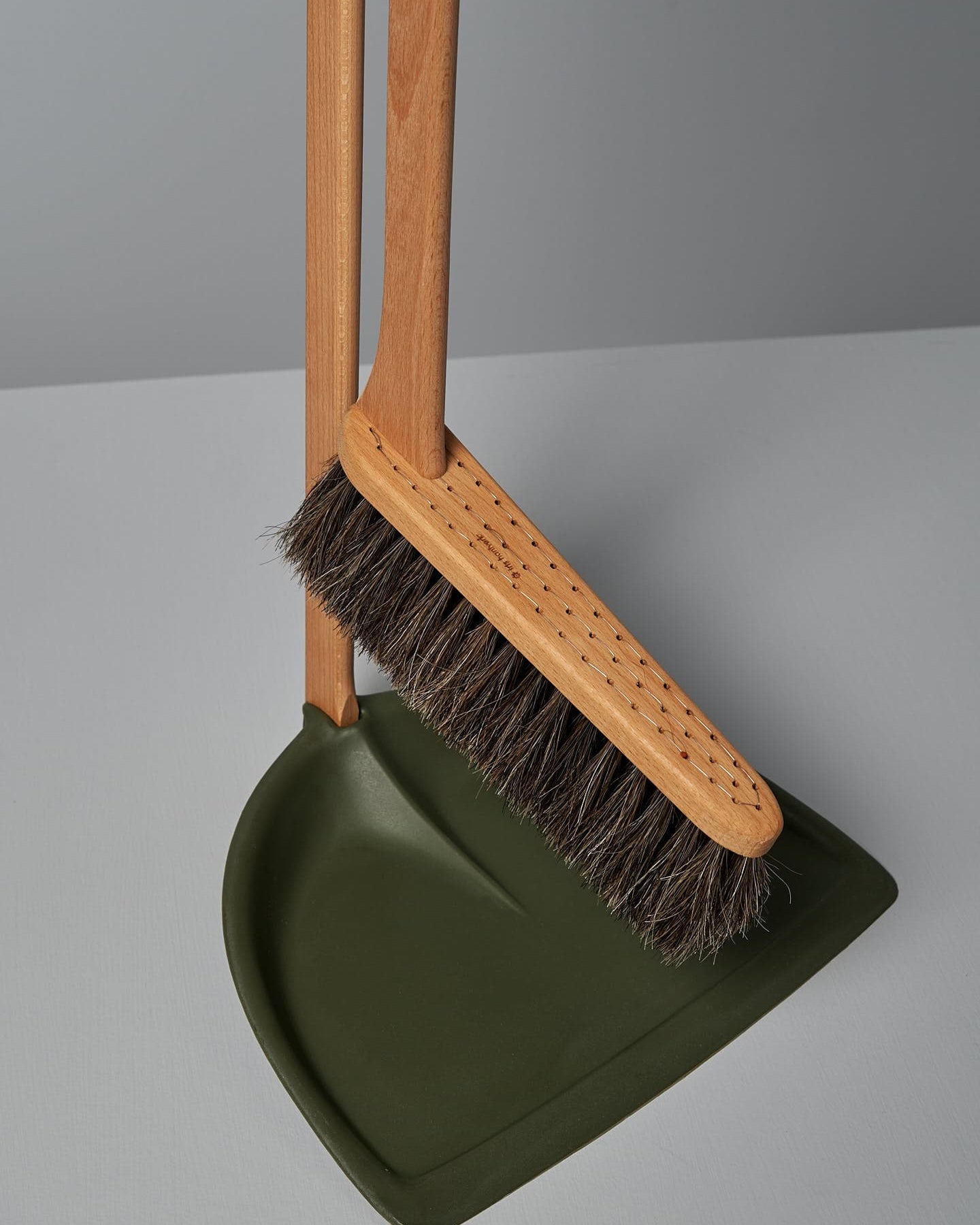 A Long Handled Dustpan & Brush Set – Moss Green from Iris Hantverk stands upright next to a green bio-polyethylene dustpan, both set against a plain gray background.