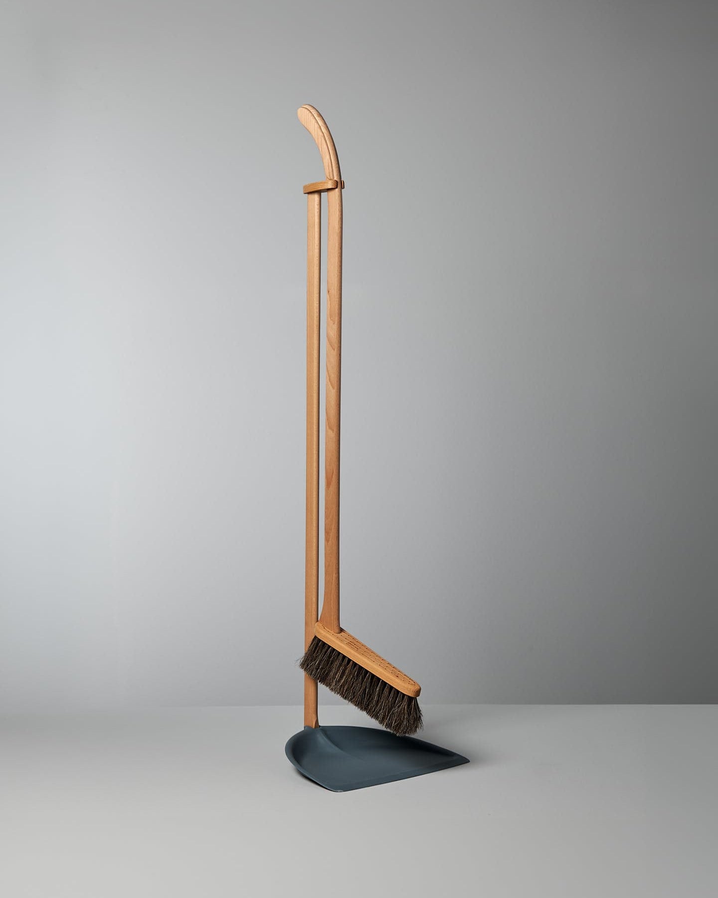 A Long Handled Dustpan & Brush Set standing upright against a plain gray background. 
