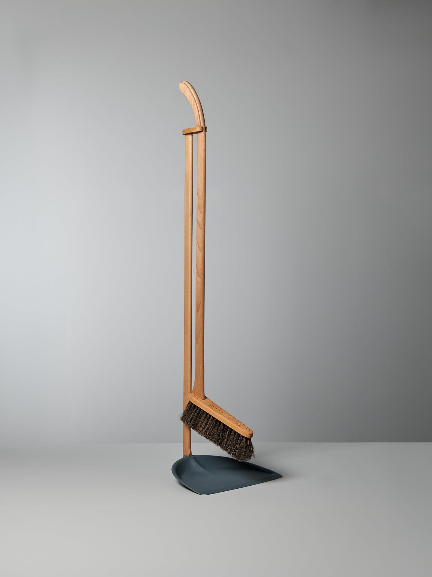 A Long Handled Dustpan & Brush Set – Petrol Blue by Iris Hantverk is standing upright against a plain gray background. Crafted by visually impaired artisans, this eco-friendly cleaning tool blends functionality and sustainability seamlessly.