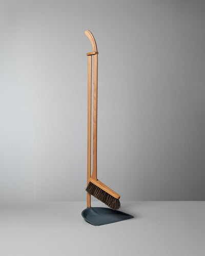 A Long Handled Dustpan & Brush Set standing upright against a plain gray background. 