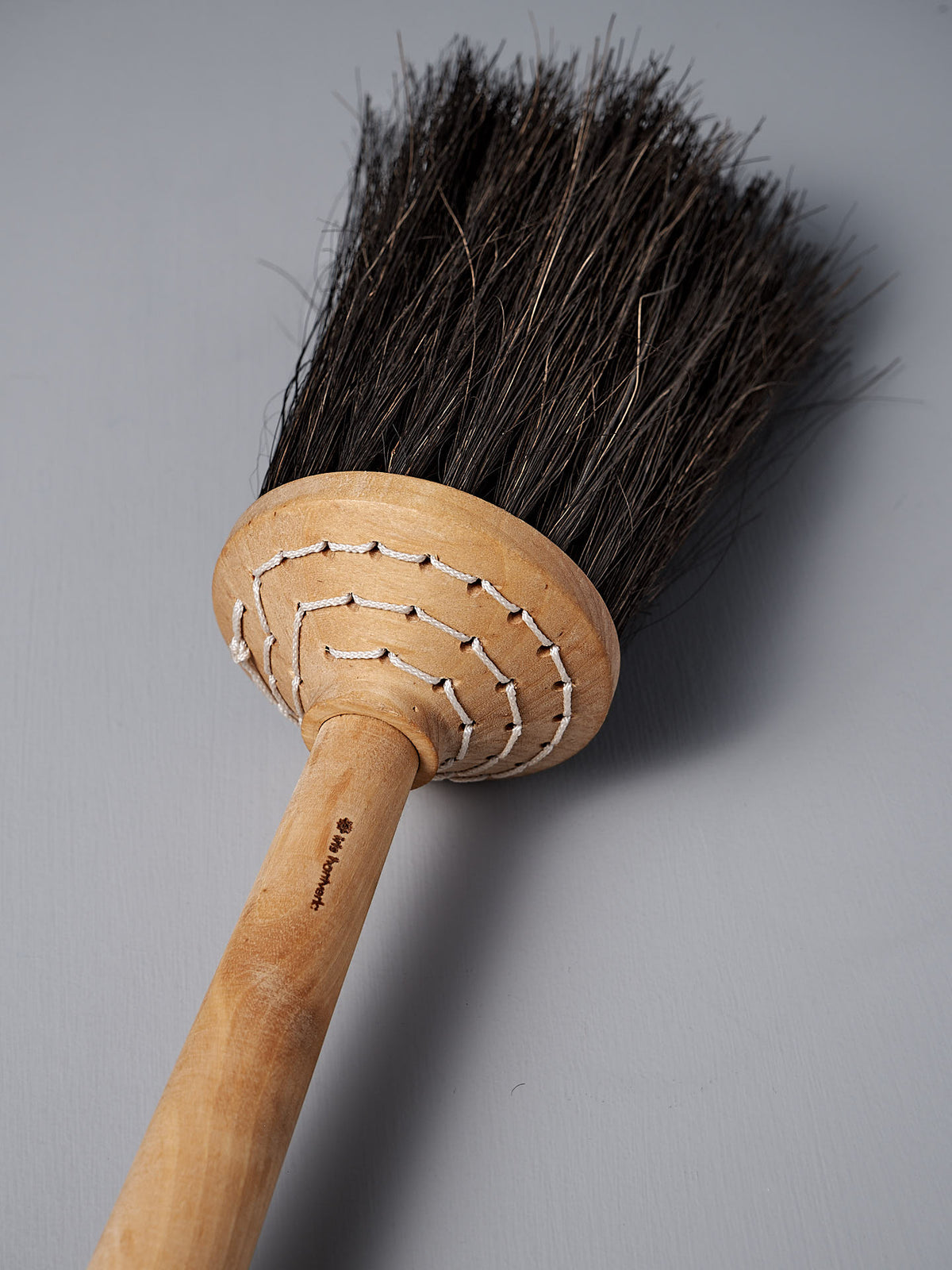 A Short Handle Porch Broom – Birch &amp; Arenga from Iris Hantverk, featuring arenga bristles and a wooden handle, lies on a gray surface.