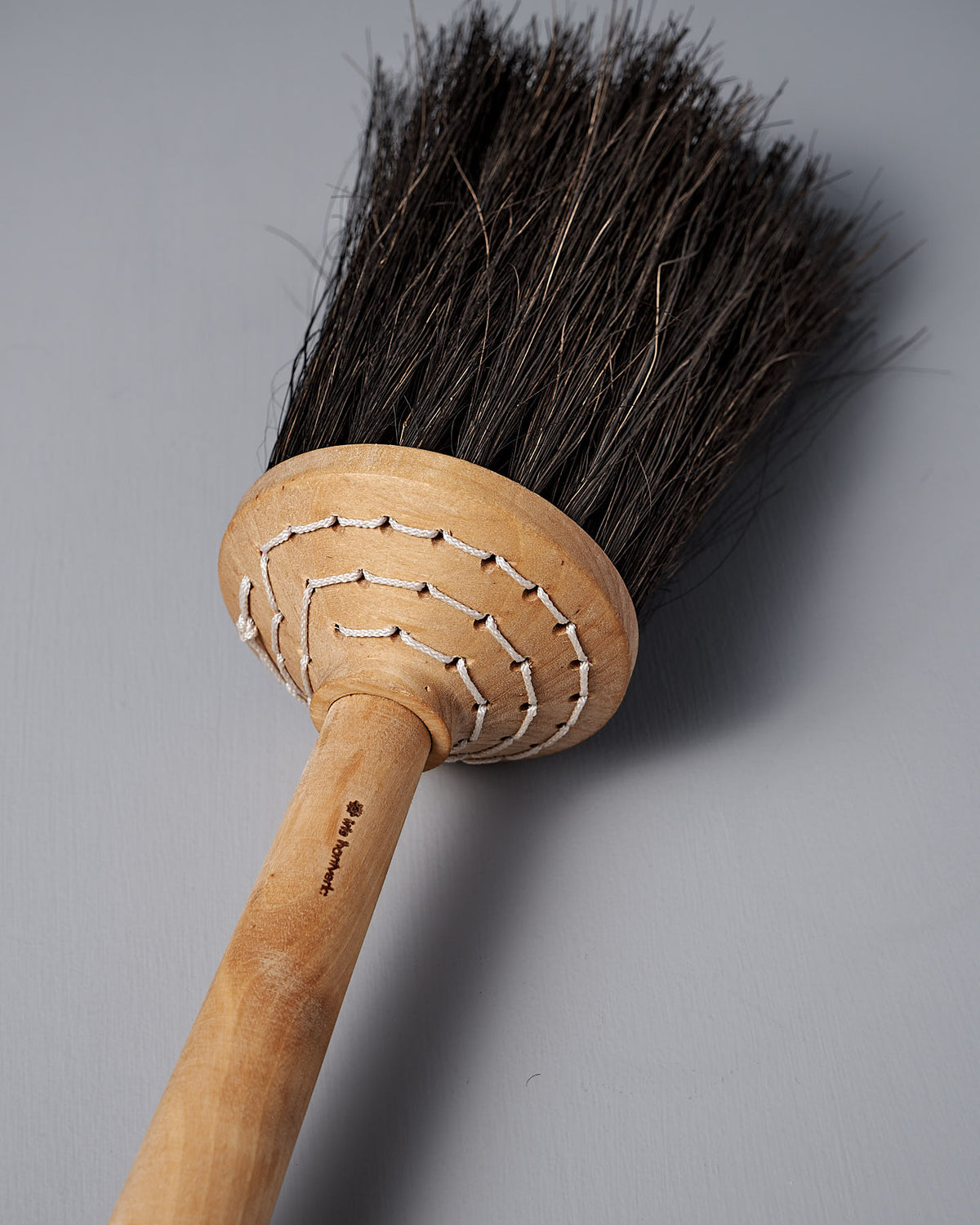 A Short Handle Porch Broom – Birch & Arenga from Iris Hantverk, featuring arenga bristles and a wooden handle, lies on a gray surface.