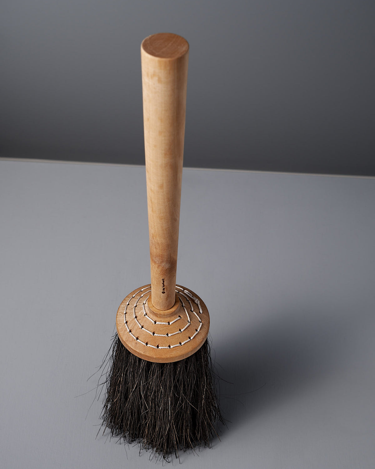 An Iris Hantverk Short Handle Porch Broom, made with birch wood and Arenga bristles, stands elegantly upright on a gray surface.