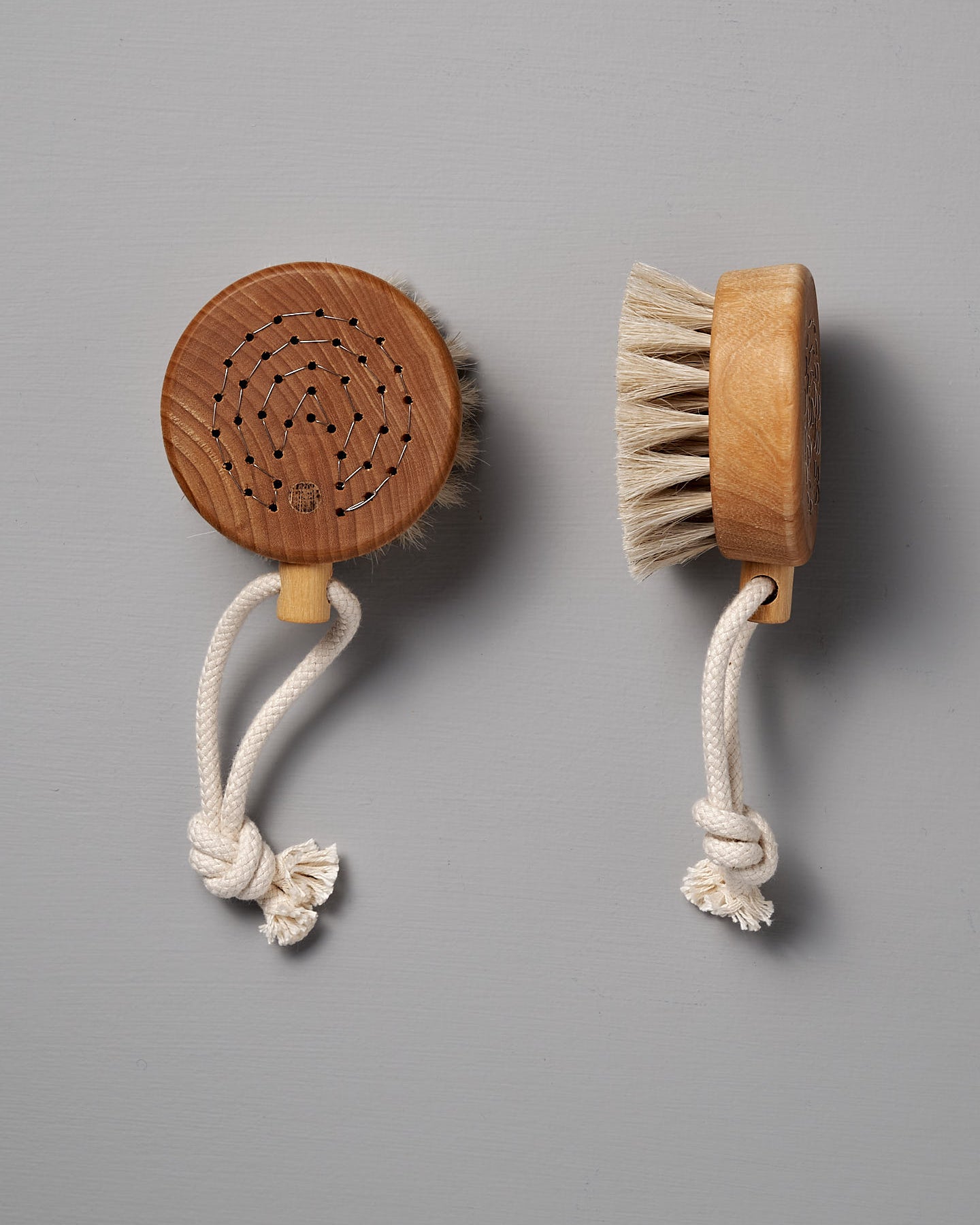 Two Puck Bath Brushes from Iris Hantverk, featuring horsehair bristles and knotted rope handles, are elegantly displayed against a gray background. These remarkable items reflect the exceptional craftsmanship associated with Iris Hantverk.