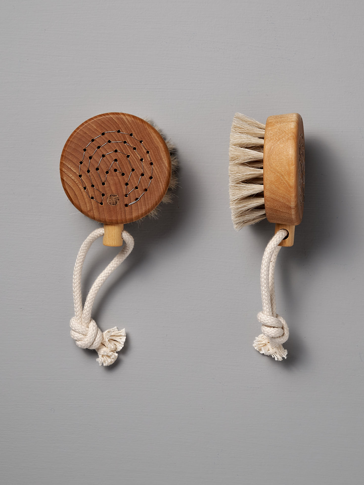Two Puck Bath Brushes from Iris Hantverk, featuring horsehair bristles and knotted rope handles, are elegantly displayed against a gray background. These remarkable items reflect the exceptional craftsmanship associated with Iris Hantverk.
