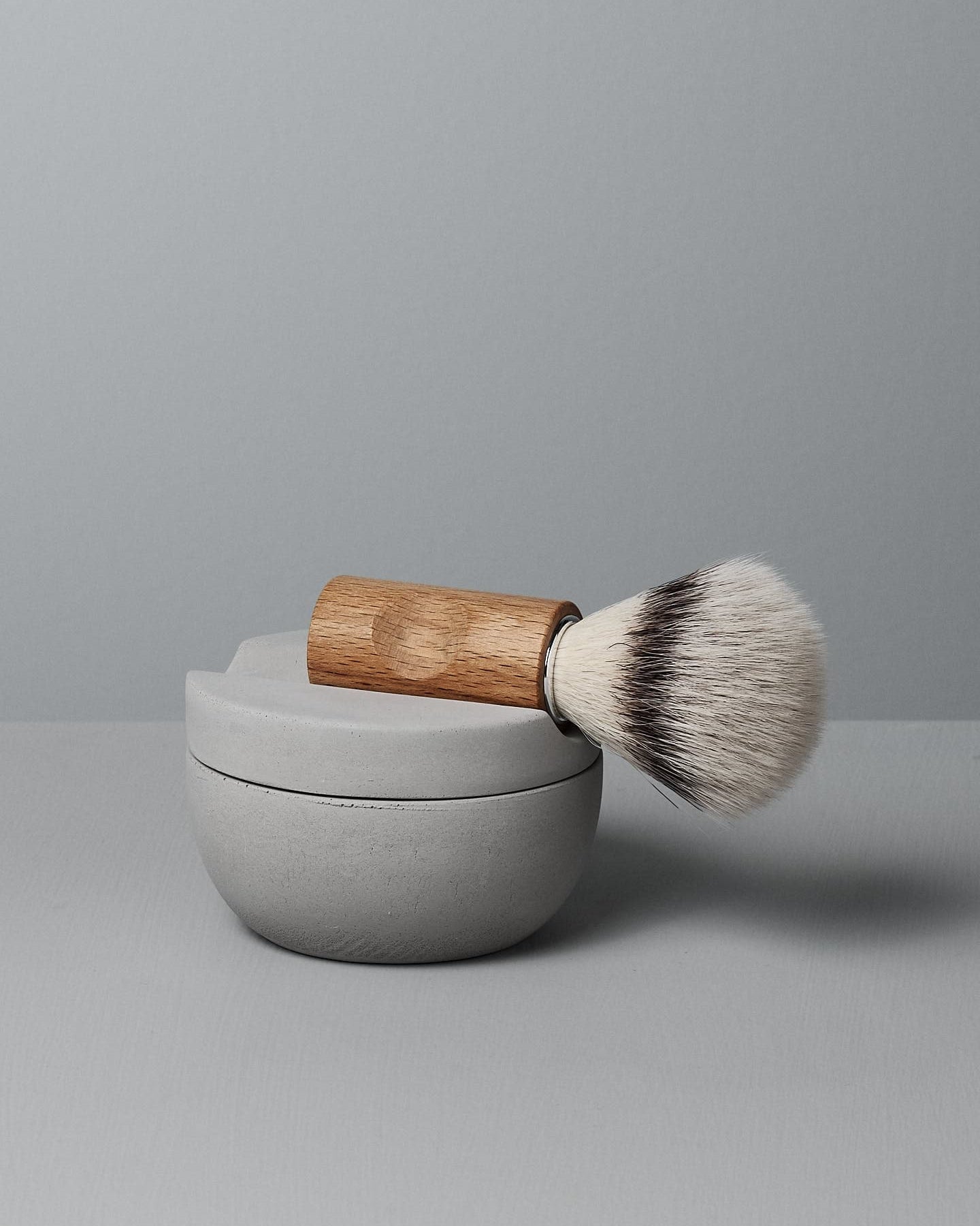 The Iris Hantverk Shaving Brush & Cup Set with Cedarwood Soap – Bundle is shown, featuring a wooden-handled brush atop a round cedarwood soap container, set against a plain gray background.