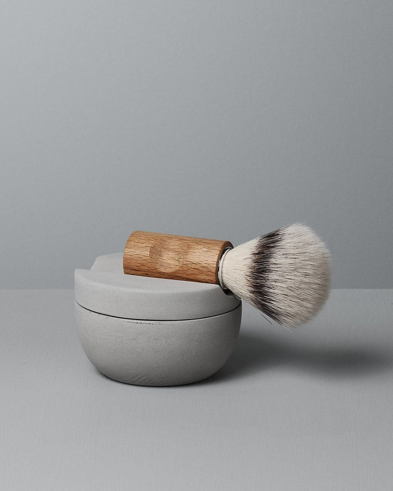 The Iris Hantverk Shaving Brush & Cup Set with Cedarwood Soap – Bundle is shown, featuring a wooden-handled brush atop a round cedarwood soap container, set against a plain gray background.