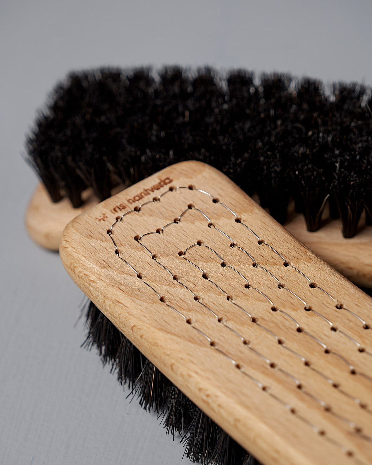 Close-up of two Iris Hantverk Shoe Brushes made from beech wood with dark horse hair bristles, set against a light gray background.