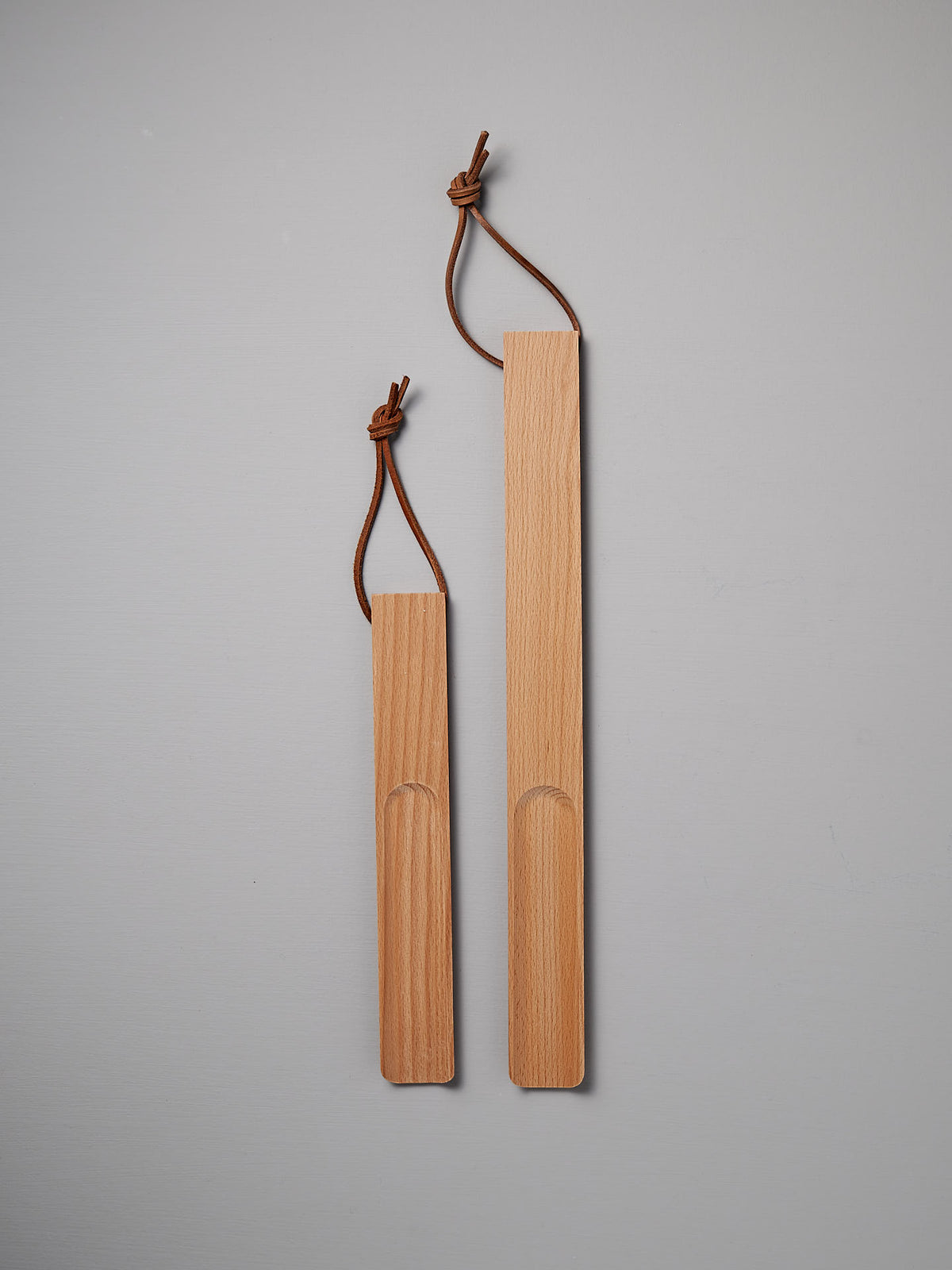 The expertly crafted Shoe Horn – Short and Long, made by Iris Hantverk from oiled beech, come with leather loops for easy hanging. Displayed with elegance on a light gray background, they include one large and one small shoehorn.