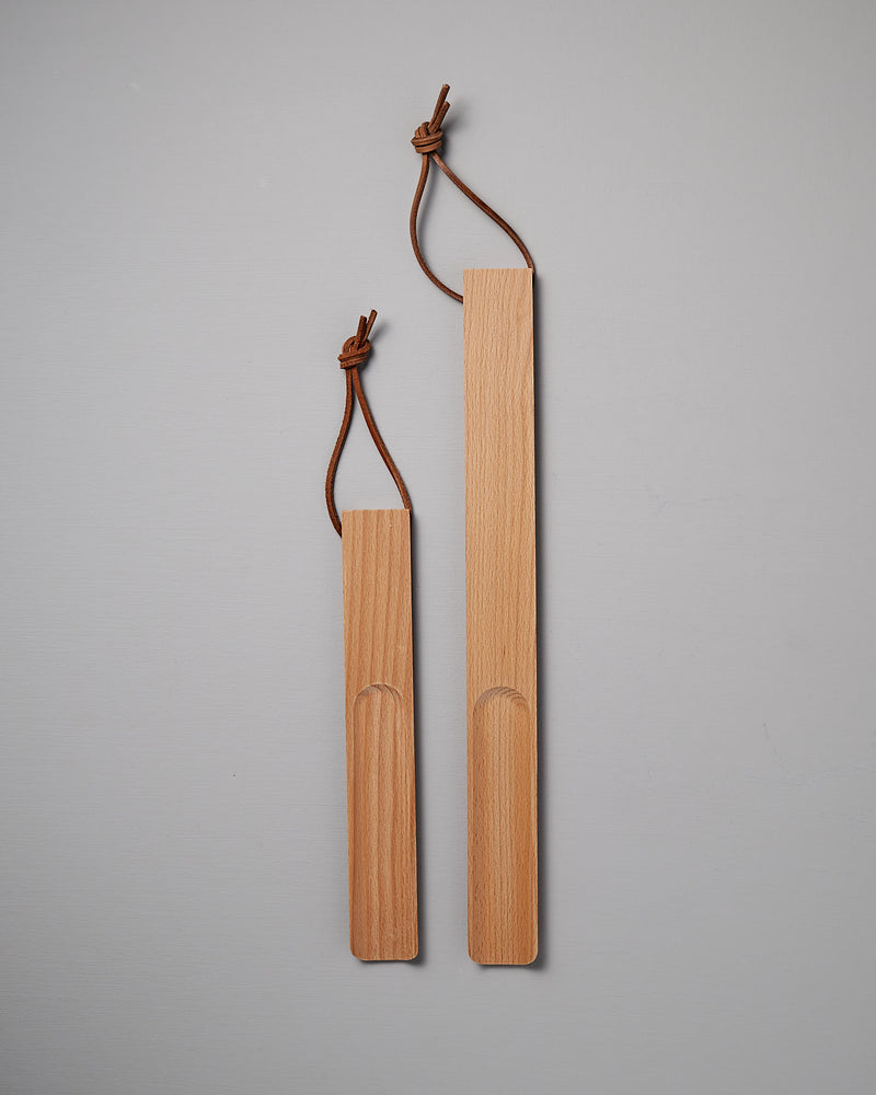 The expertly crafted Shoe Horn – Short and Long, made by Iris Hantverk from oiled beech, come with leather loops for easy hanging. Displayed with elegance on a light gray background, they include one large and one small shoehorn.