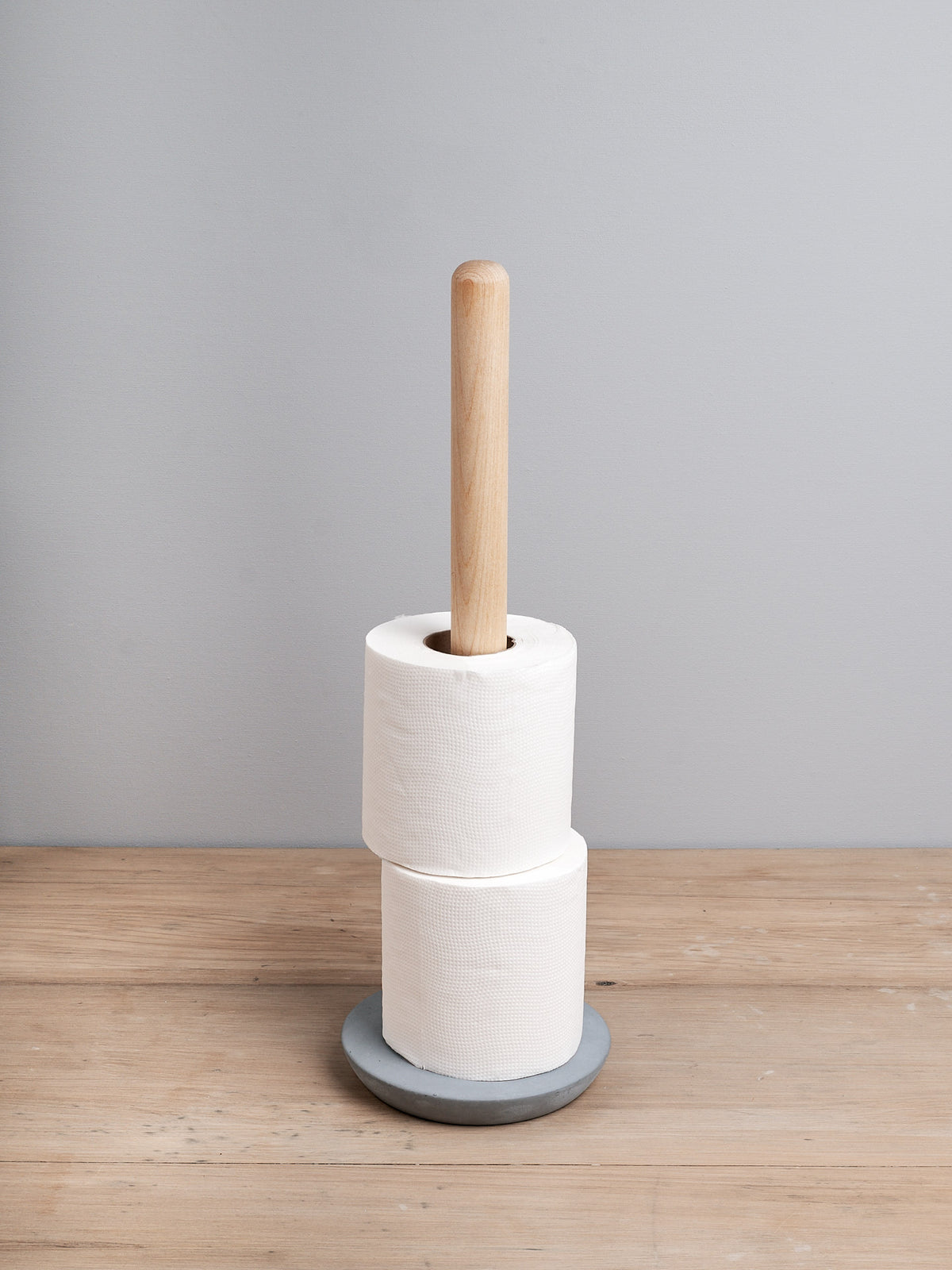 A roll of paper towels on an Iris Hantverk Toilet Brush + Toilet Roll Holder Set against a grey background.