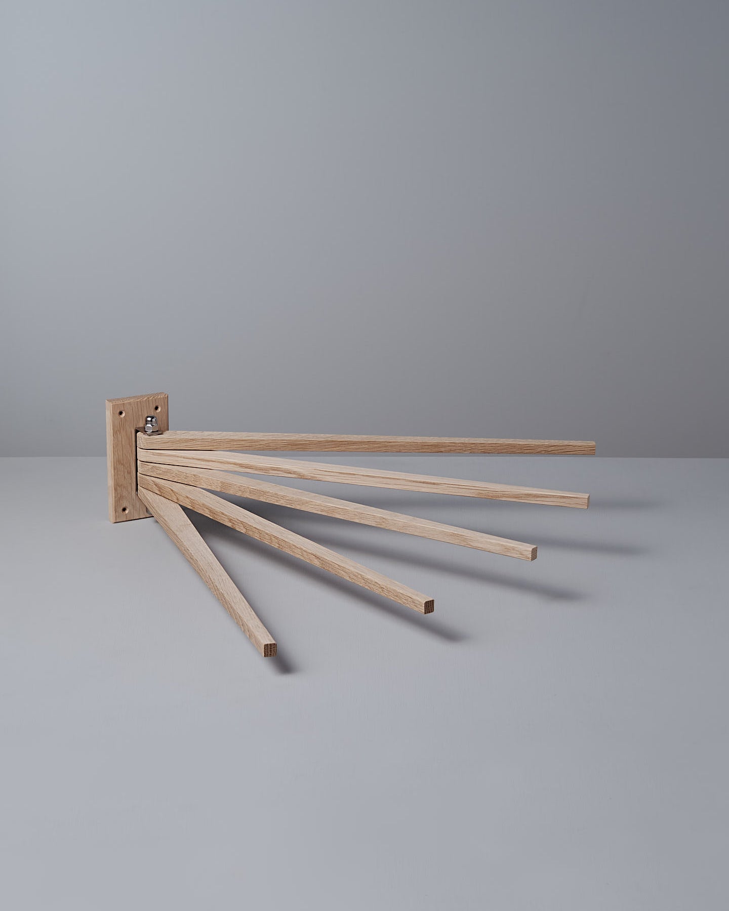 The Oak Towel Drying Rack – 5 Arm by Iris Hantverk, made from solid oak, is mounted on a wall with a plain gray background.