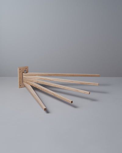 The Oak Towel Drying Rack – 5 Arm by Iris Hantverk, made from solid oak, is mounted on a wall with a plain gray background.