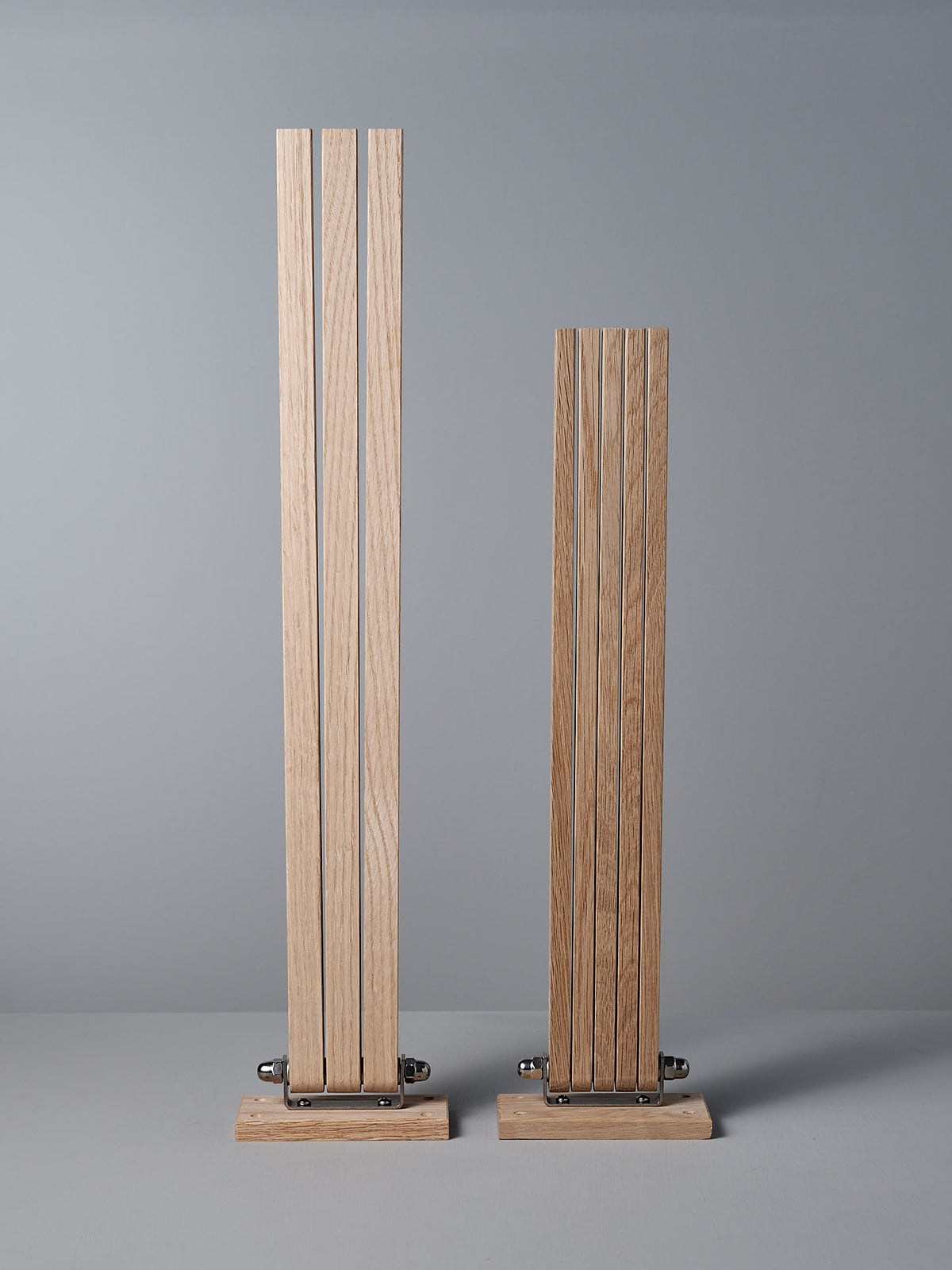 Constructed from solid oak, the Oak Towel Drying Rack – 3 Arm by Iris Hantverk showcases a sophisticated design with vertical slats set on rectangular bases at varying heights. This piece easily complements any interior style and stands elegantly against a simple backdrop.