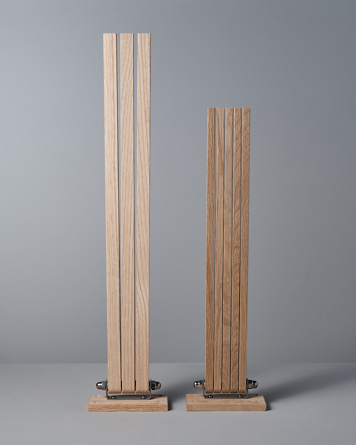 The Oak Towel Drying Rack – 5 Arm by Iris Hantverk, featuring two sets of vertically aligned wooden slats with hinges, stands on a light surface against a gray background.