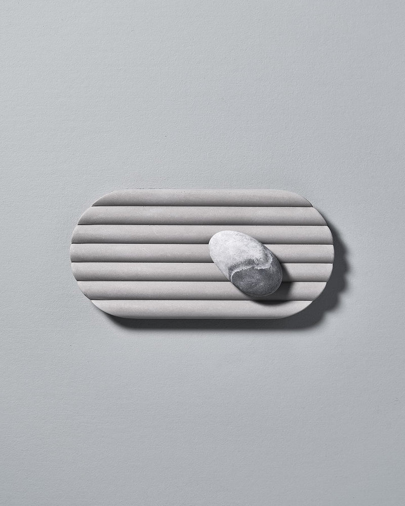 A Concrete Tray by Iris Hantverk with a white marble on it.