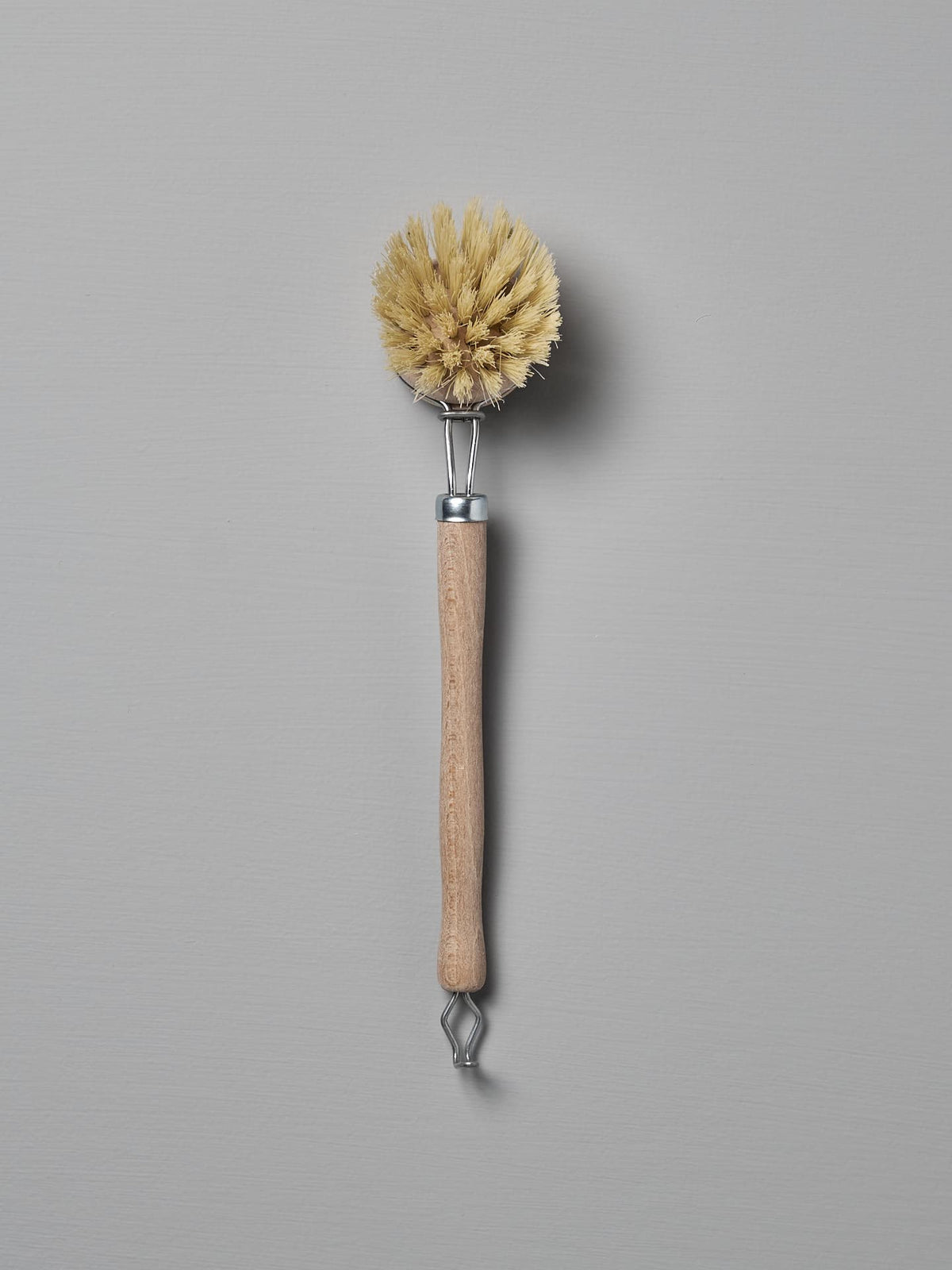 An Iris Hantverk Dish Brush with Replaceable Head, featuring a wooden handle and stiff yellow bristles made from durable Tampico fibre, shown against a plain grey background.