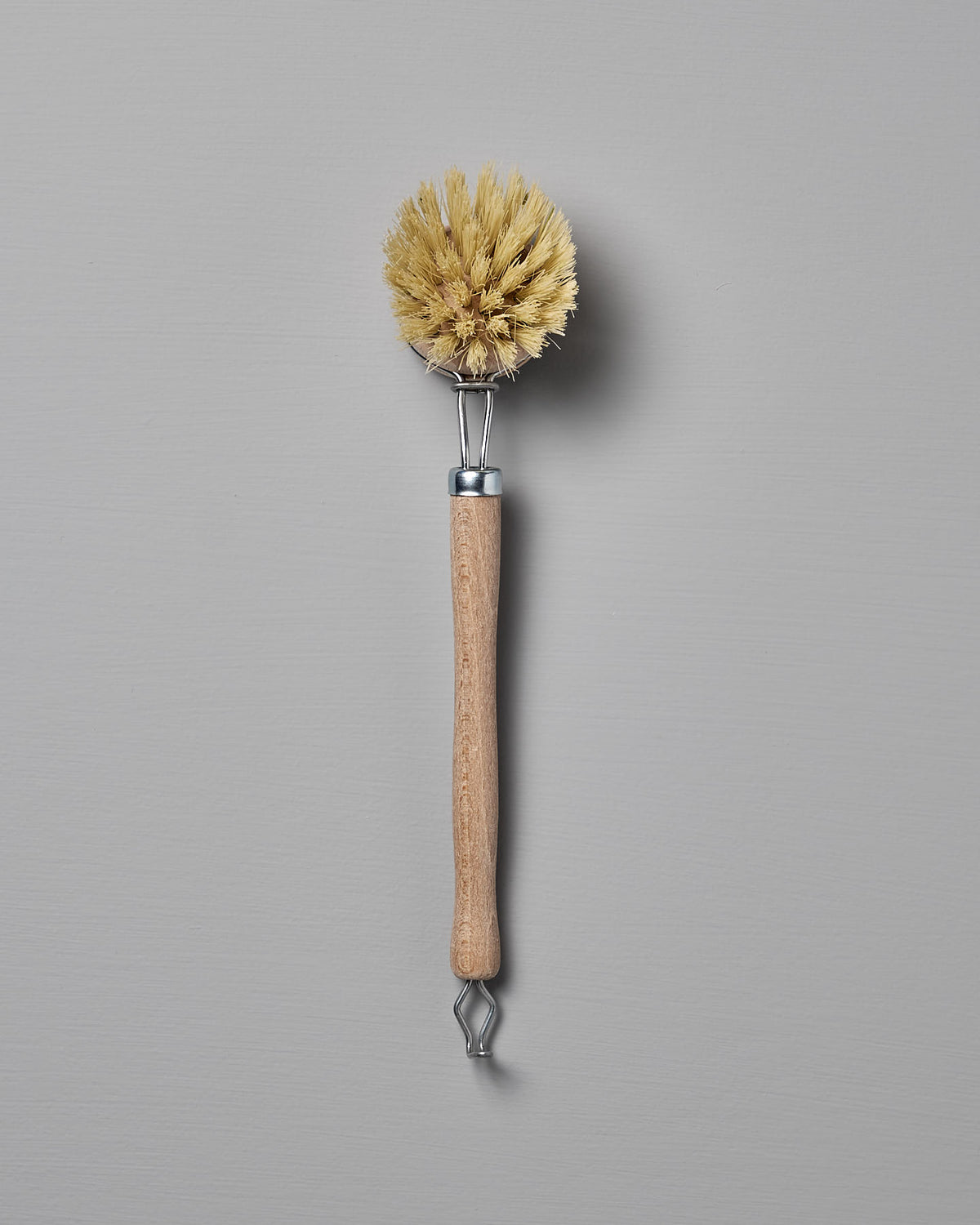 An Iris Hantverk Dish Brush with Replaceable Head, featuring a wooden handle and stiff yellow bristles made from durable Tampico fibre, shown against a plain grey background.