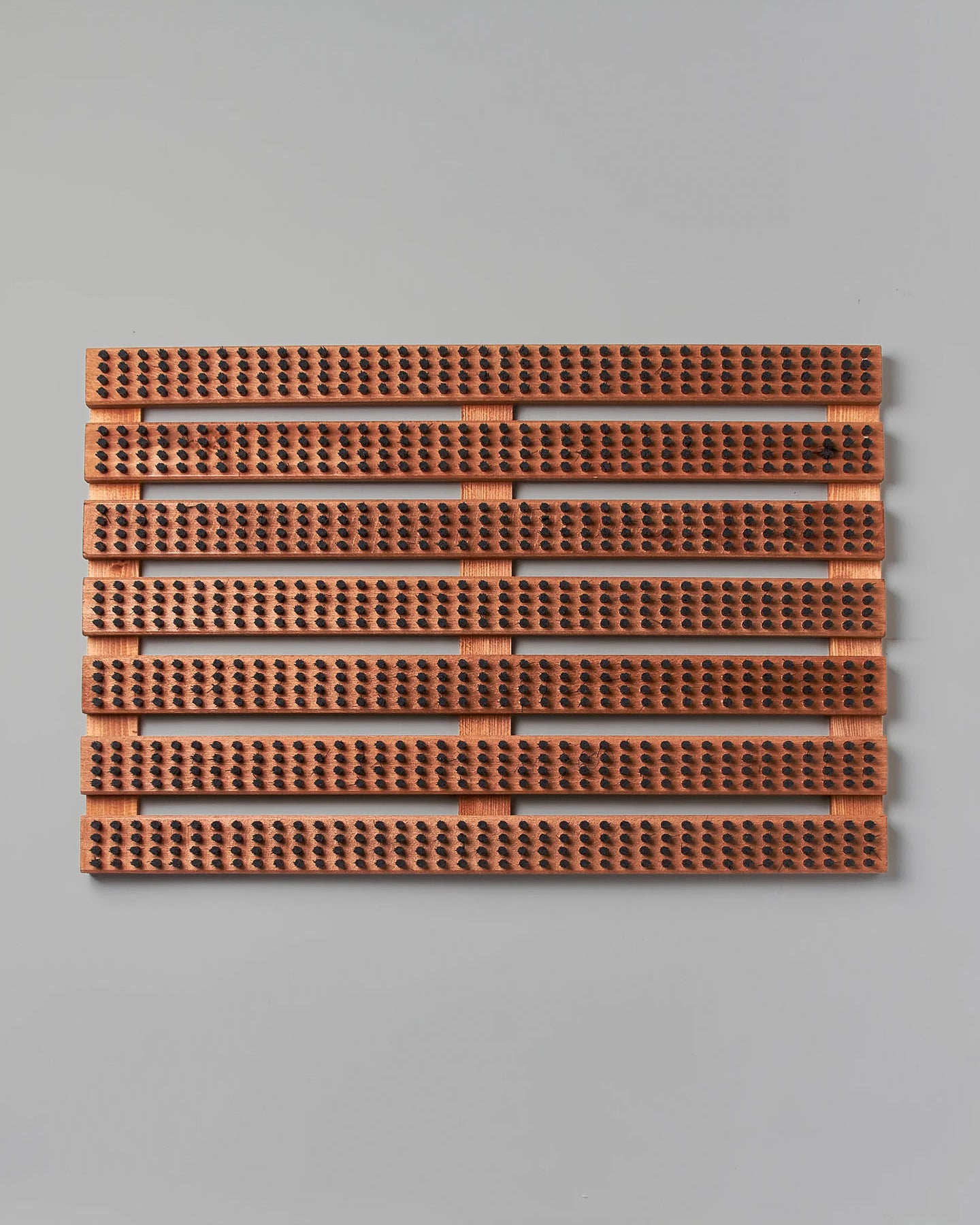 A rectangular panel of brown acoustic tiles with a ribbed texture and perforations, elegantly enhanced by its Beechwood base, is mounted on a light gray wall. Featuring quality craftsmanship reminiscent of the Iris Hantverk brand's Wooden Doormat with Bristles – Standard.