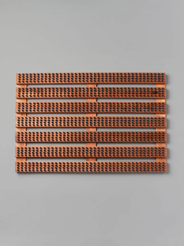 A rectangular panel of brown acoustic tiles with a ribbed texture and perforations, elegantly enhanced by its Beechwood base, is mounted on a light gray wall. Featuring quality craftsmanship reminiscent of the Iris Hantverk brand's Wooden Doormat with Bristles – Standard.
