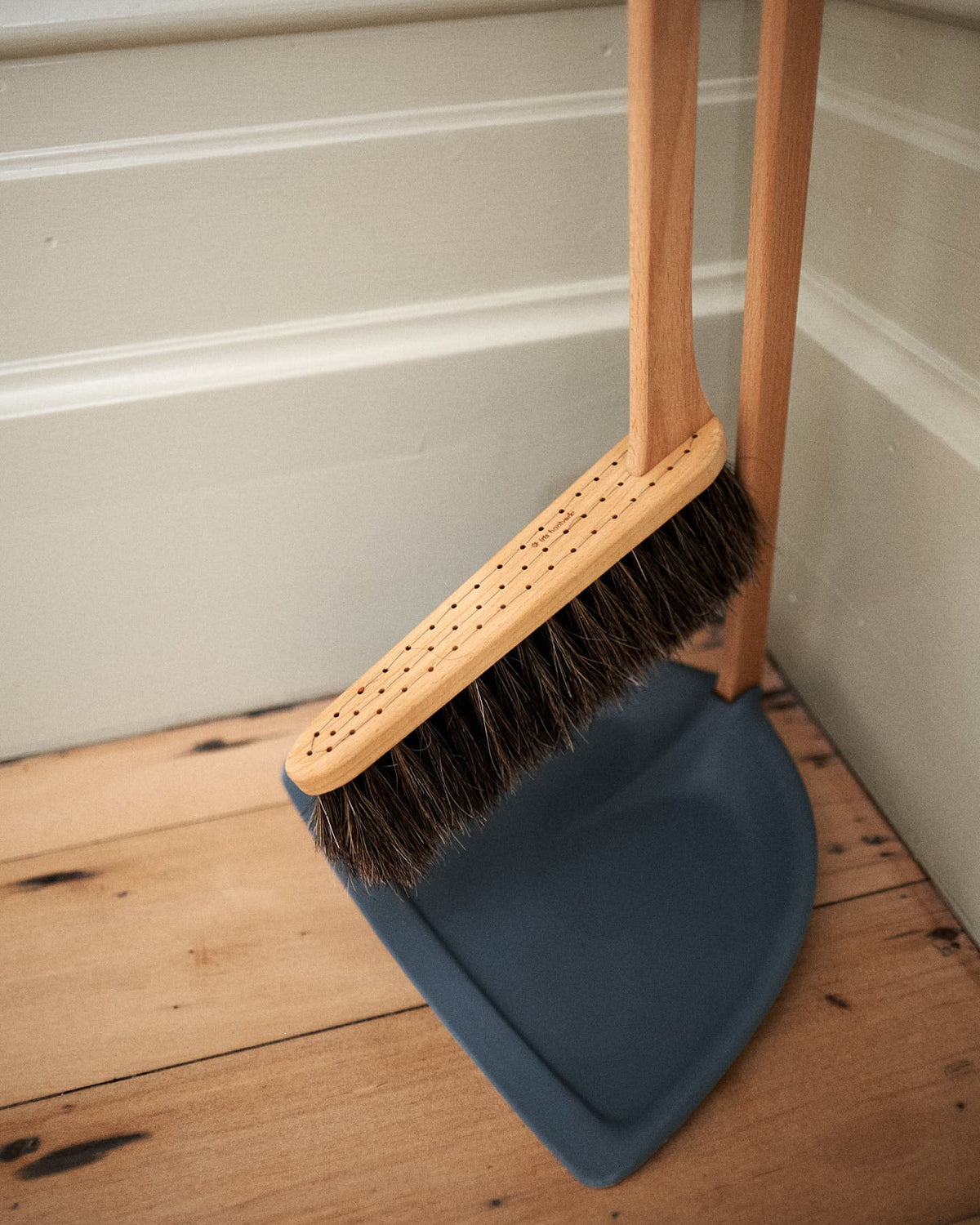 A Long Handled Dustpan & Brush Set – Petrol Blue from Iris Hantverk rests on a light-colored wall and on a wooden floor.
