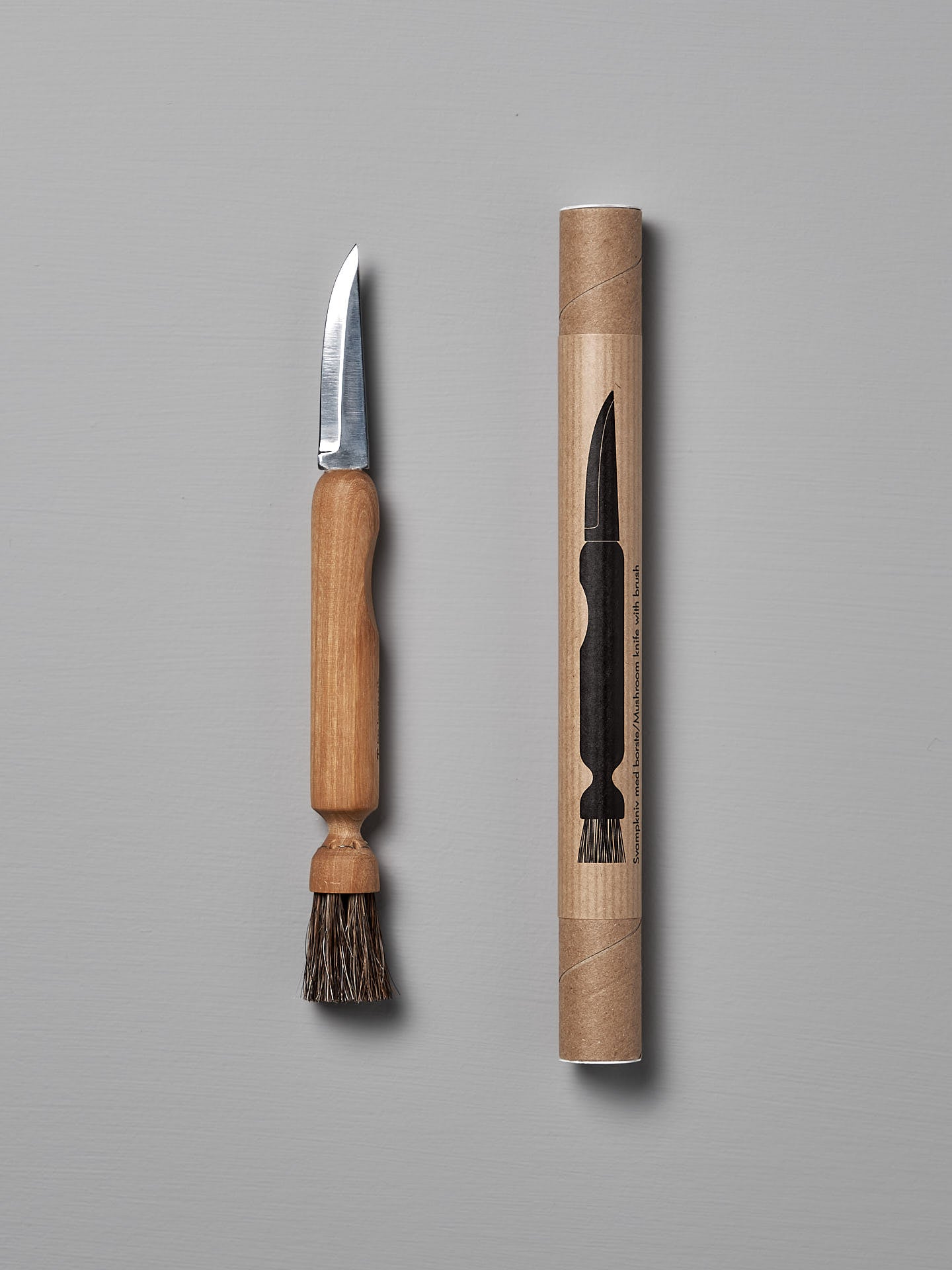 The Iris Hantverk Mushroom Brush & Knife, featuring a wooden handle and horsehair brush, is shown beside its cylindrical cardboard package with an illustration of the product.