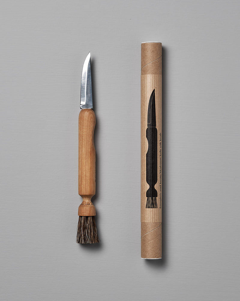 The Iris Hantverk Mushroom Brush & Knife, featuring a wooden handle and horsehair brush, is shown beside its cylindrical cardboard package with an illustration of the product.