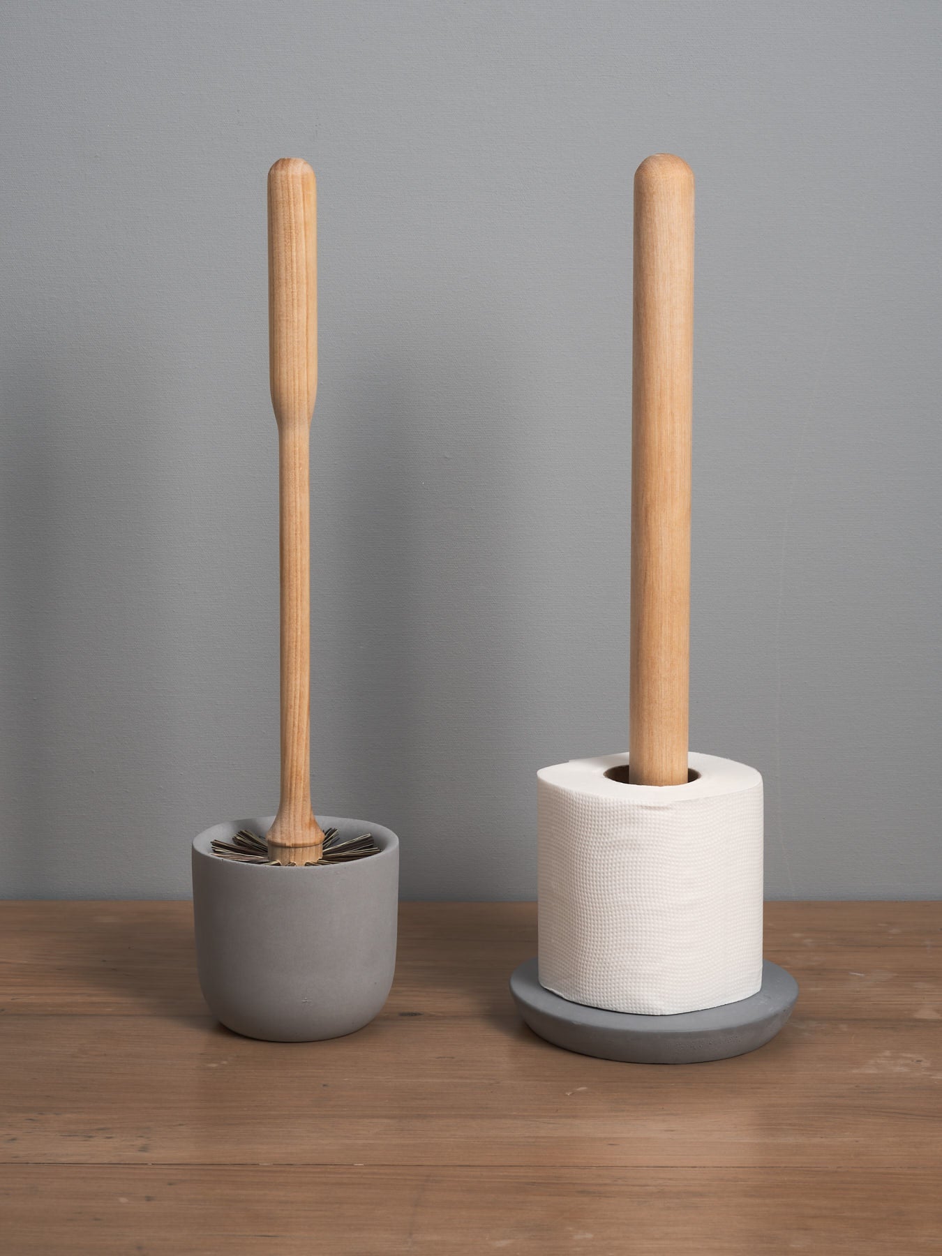 An Iris Hantverk Toilet Brush + Toilet Roll Holder Set on holders against a gray wall.