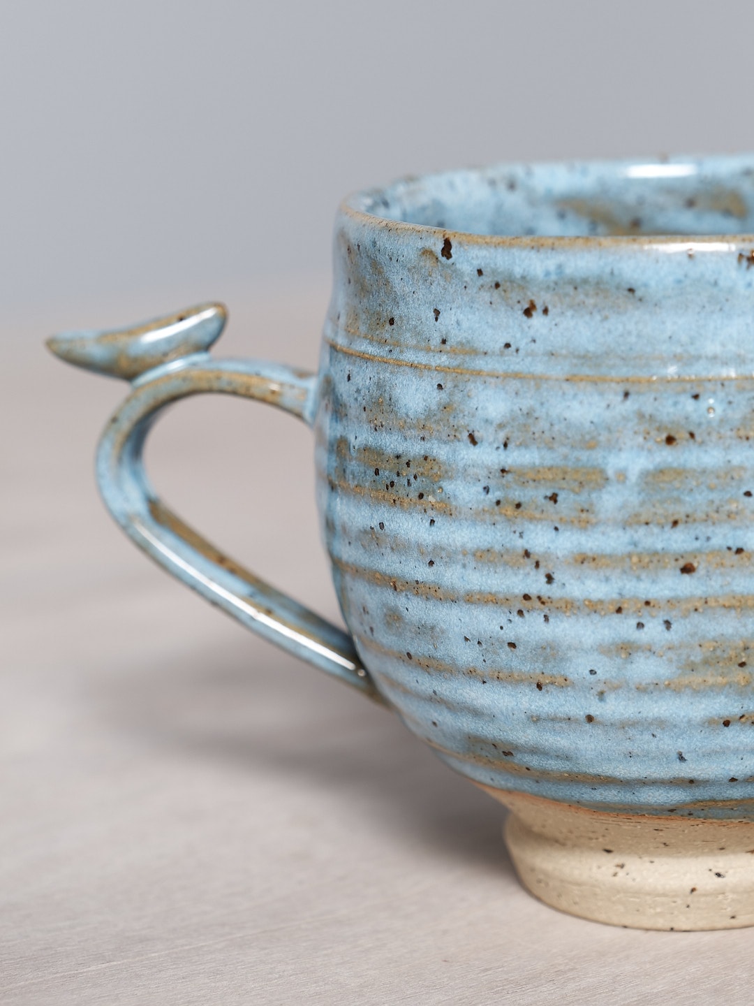 A handcrafted Bird Handle Cup - Sky Blue, by Jino Ceramic Studio, placed on a wooden table.
