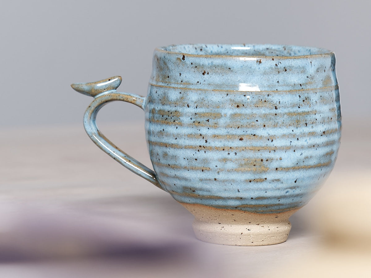 A Bird Handle Cup – Sky Blue made by Jino Ceramic Studio sitting on a table.