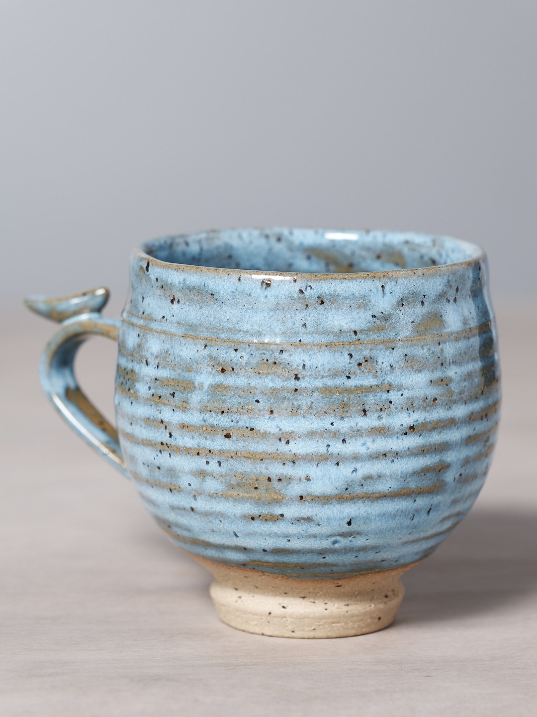 A Bird Handle Cup - Sky Blue by Jino Ceramic Studio placed on a wooden table.