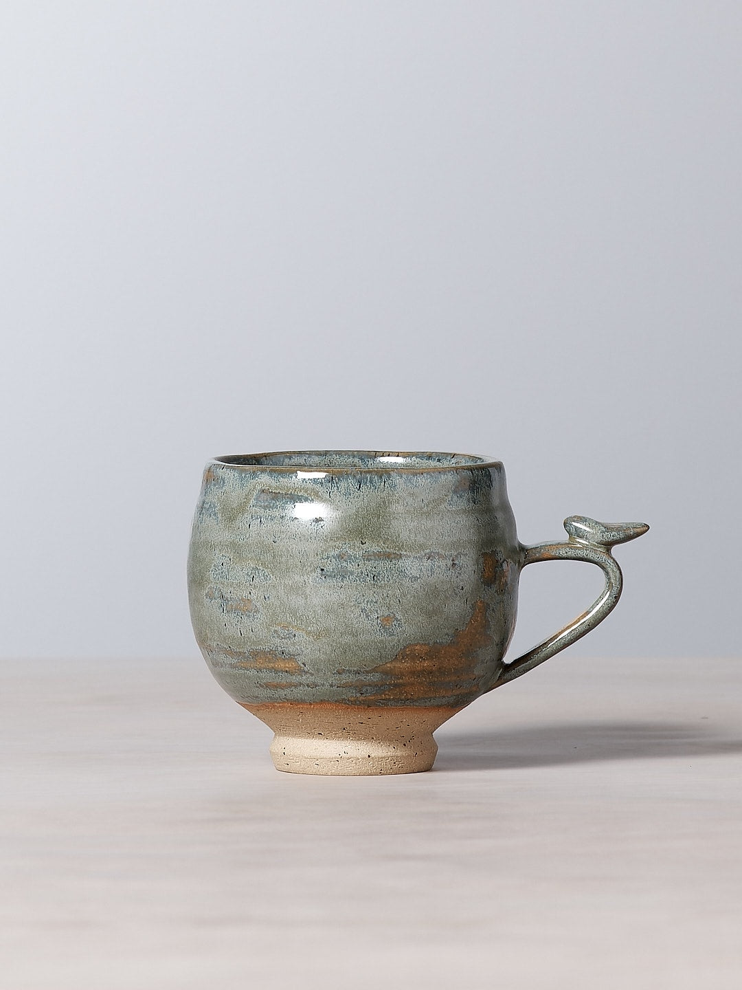 A handmade Bird Handle Cup – Green Tea by Jino Ceramic Studio on a table.
