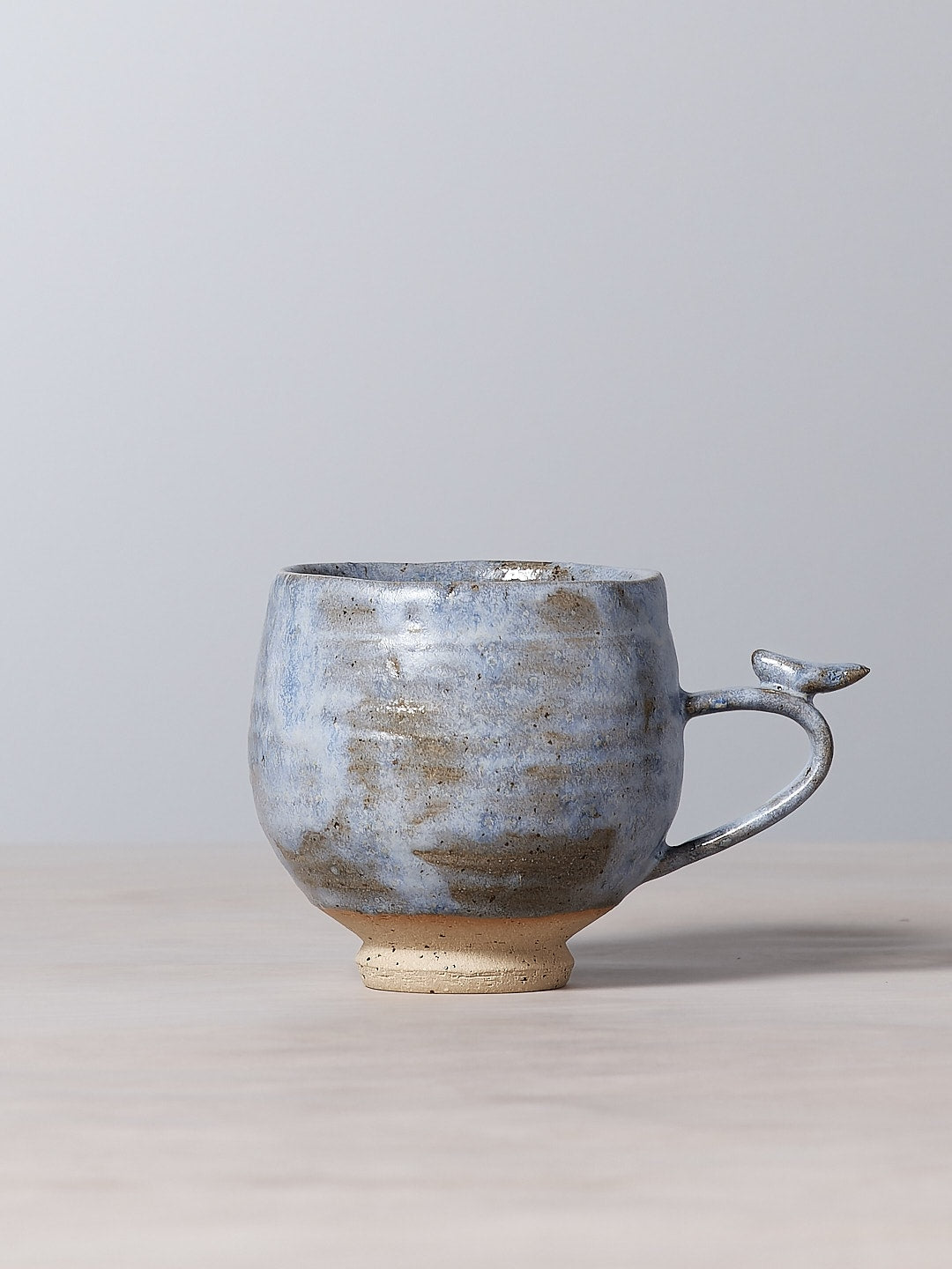 A small handmade blue Bird Handle Cup – Kokako, from Jino Ceramic Studio, sitting on a table.