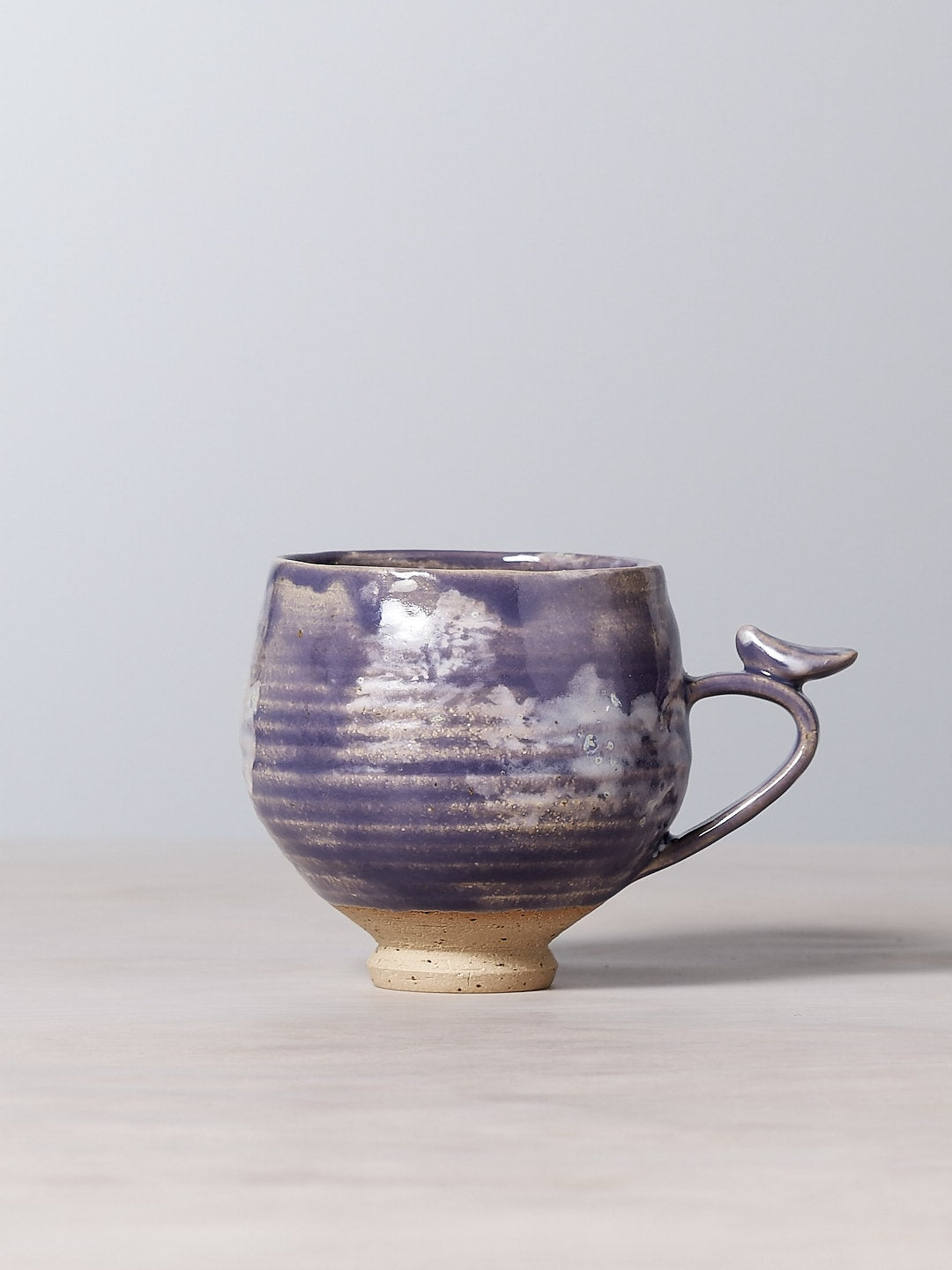 A blue and white Bird Handle Cup – Pukeko with a handle on a table, made by Jino Ceramic Studio.