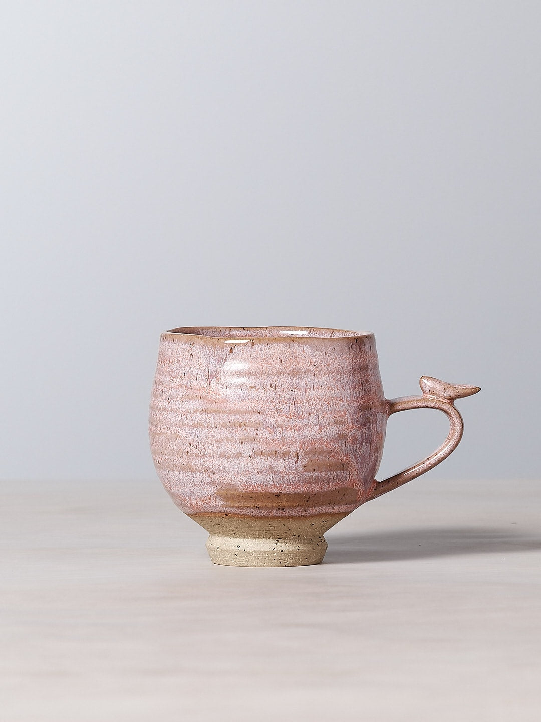 A small handmade Bird Handle Cup - Rhubarb, adorned with delicate blooms and birds, sitting on a table in New Zealand.