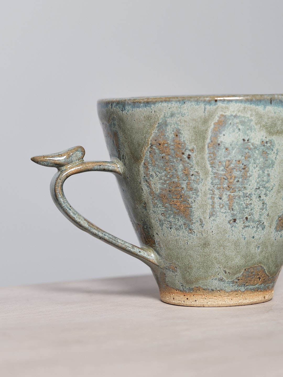 A Bird Handle Mug - Green Tea from Jino Ceramic Studio, perfect for tea-drinking, sitting on a table.