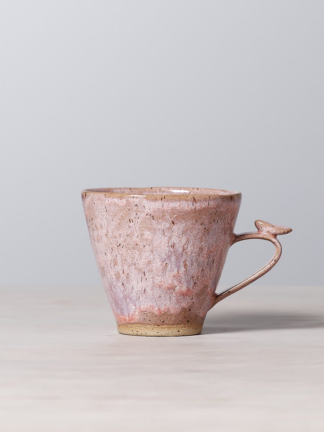 A small pink Jino Ceramic Studio Bird Handle Mug – Rhubarb sitting on a table.